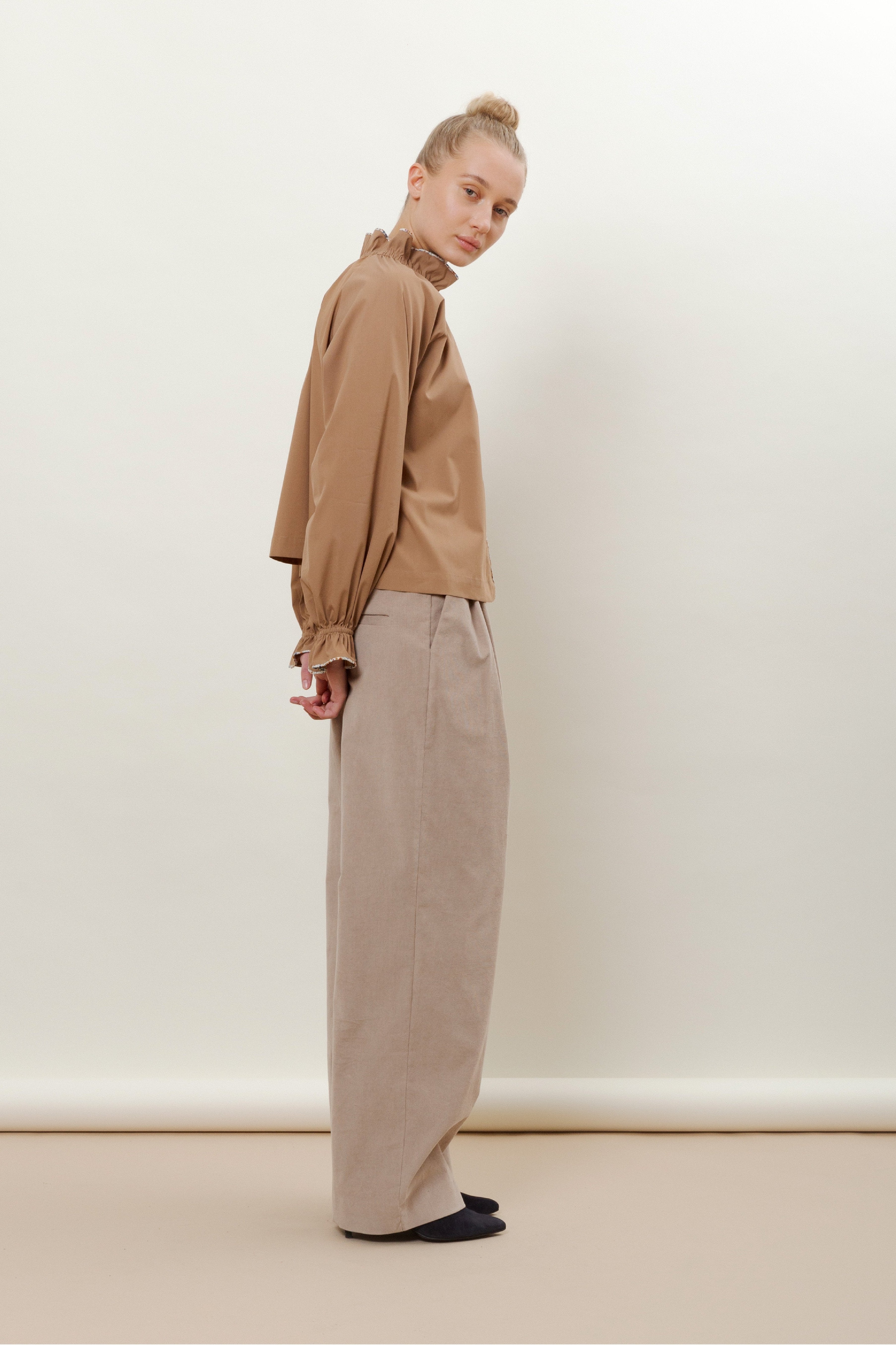 Woman in beige trousers and brown shirt with long sleeves and ruffles