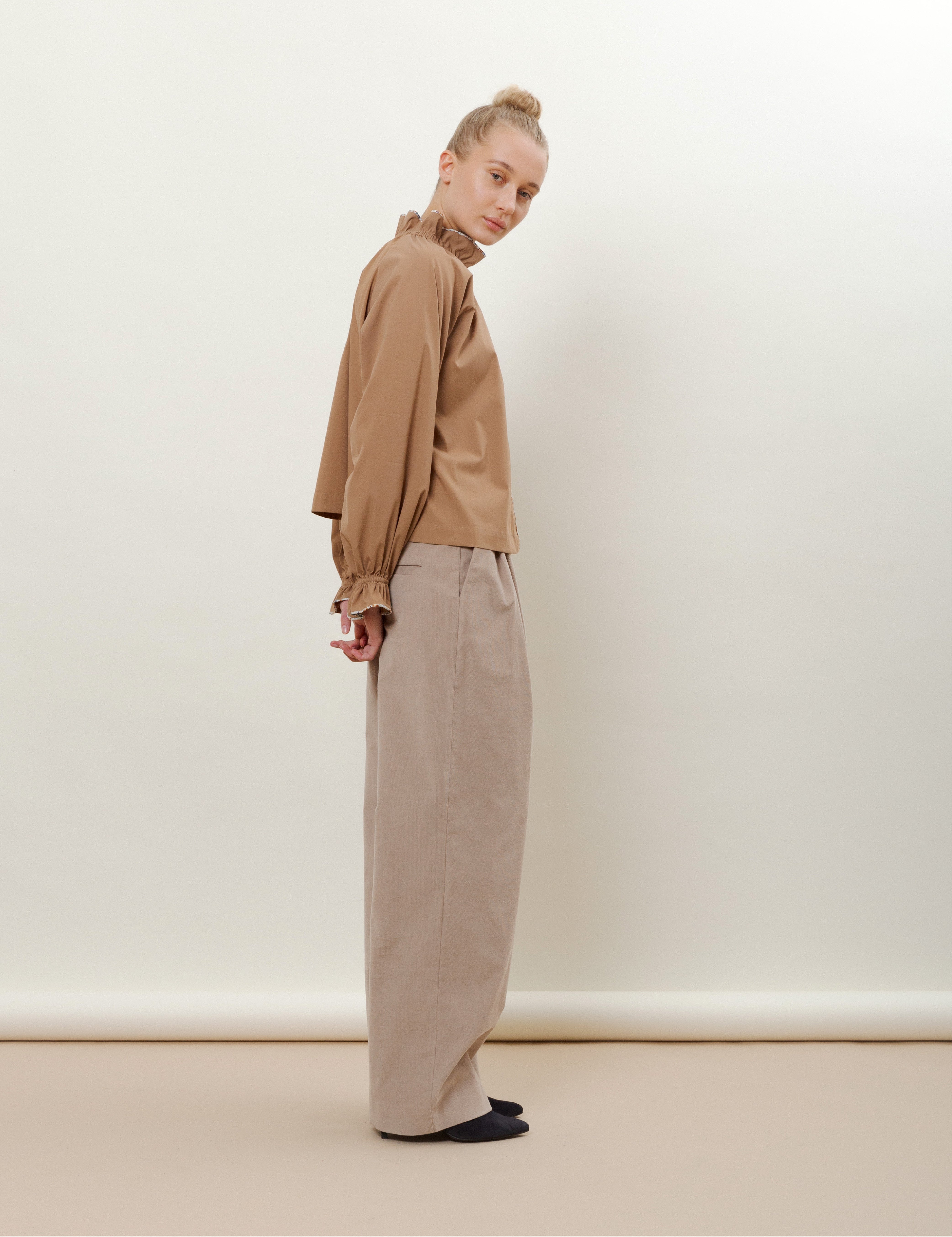 Woman in wide beige corduroy pants  and brown long sleeved shirt with frilled neck and cuffs