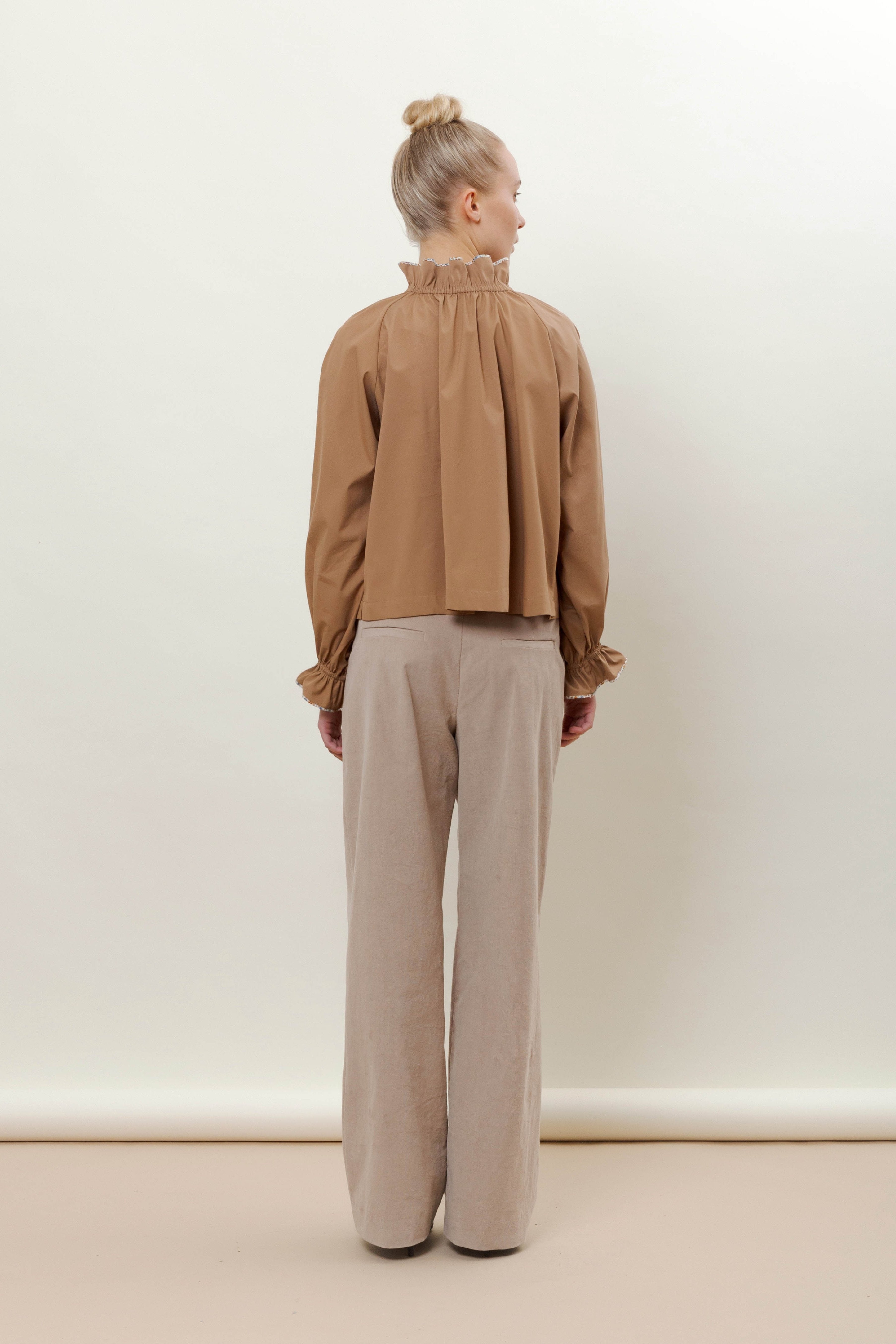 Woman in beige trousers and brown shirt with long sleeves and ruffles