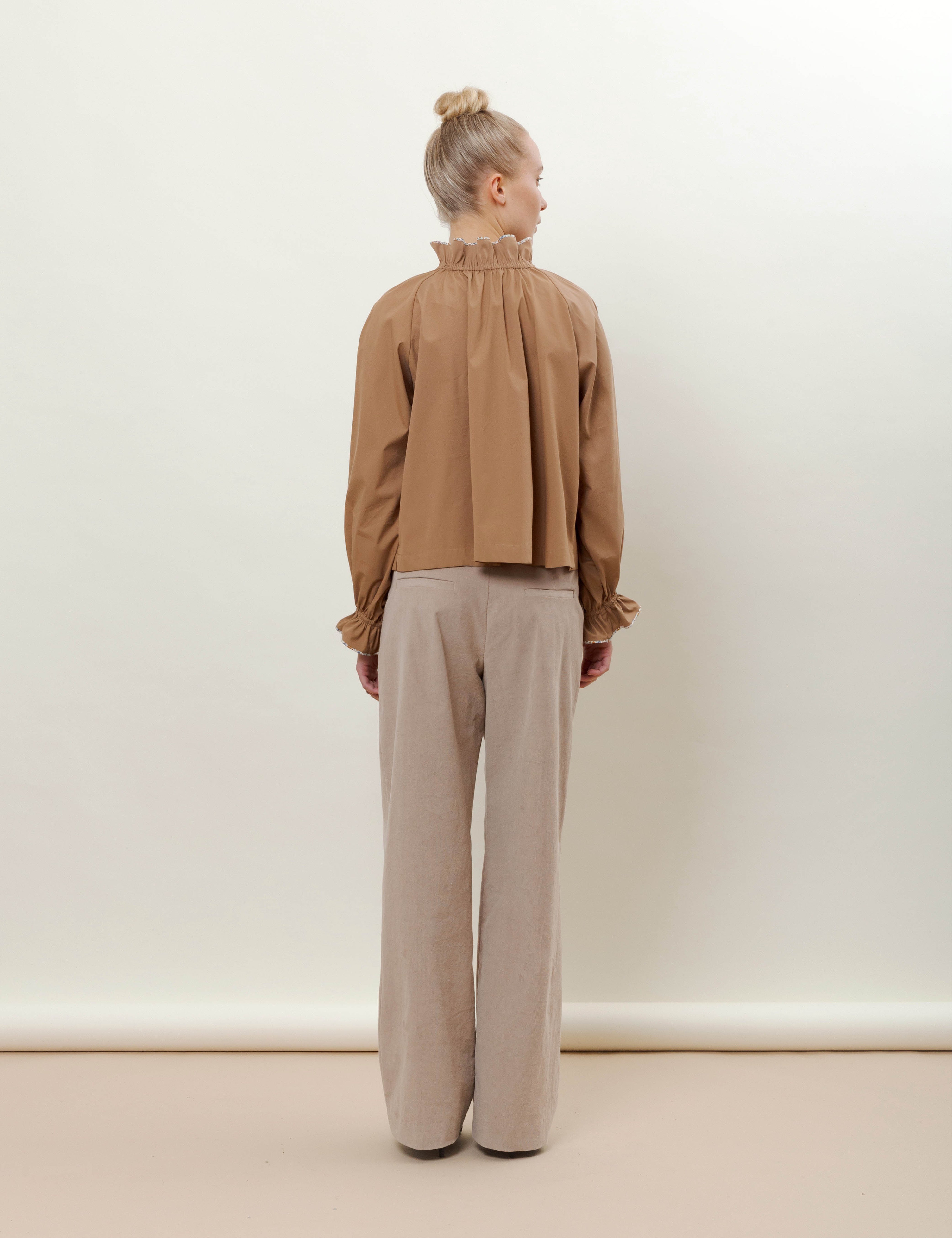 Woman in wide beige corduroy pants  and brown long sleeved shirt with frilled neck and cuffs