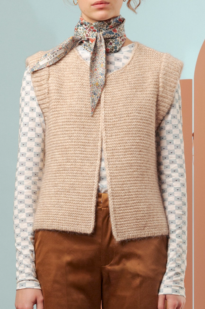 Woman in blue and white patterned t-shirt, beige knitted wool vest, scarf and brown pants