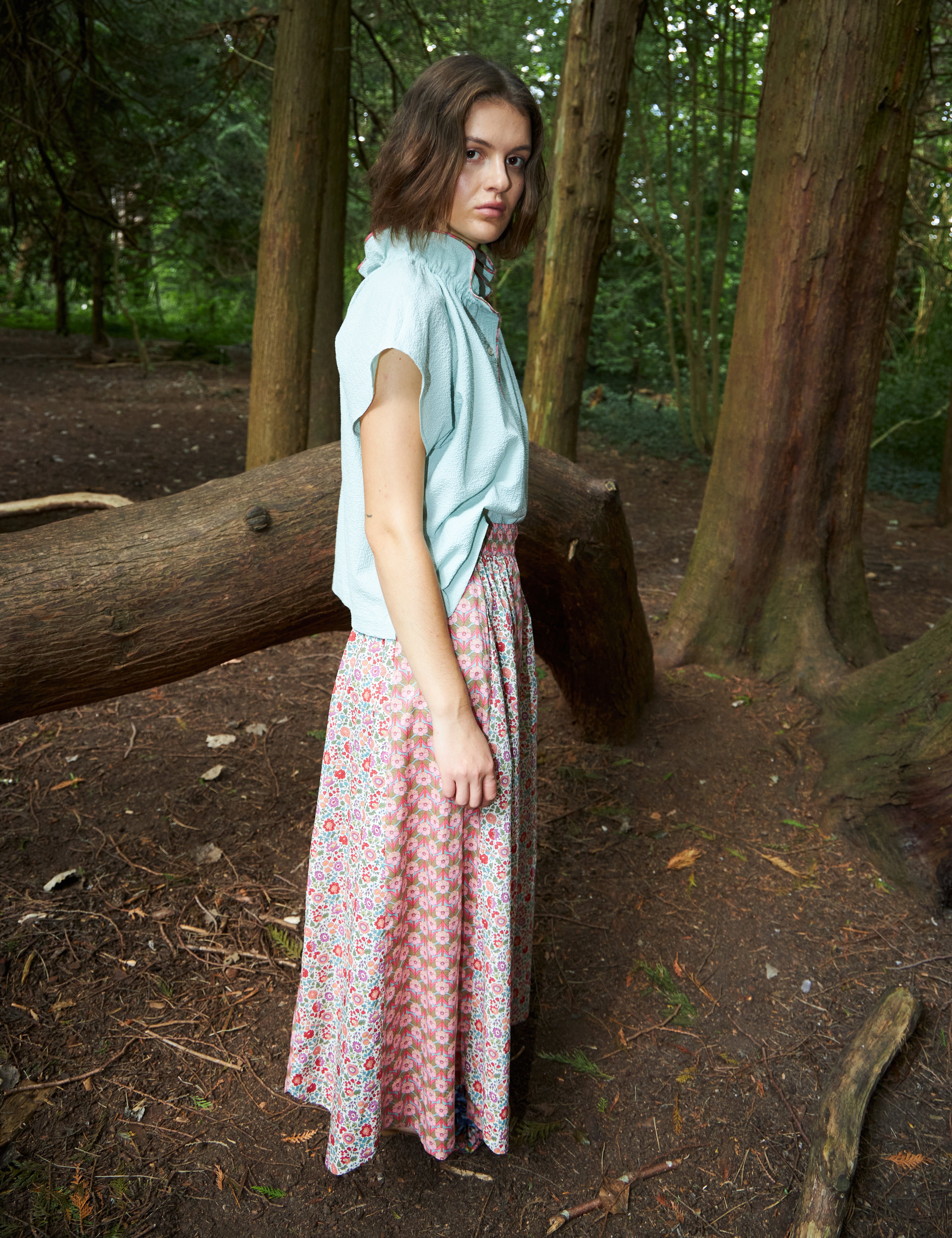 Woman in maxi skirt with two different floral prints in pink red and green and blue sleeveless top with frilled stand collar