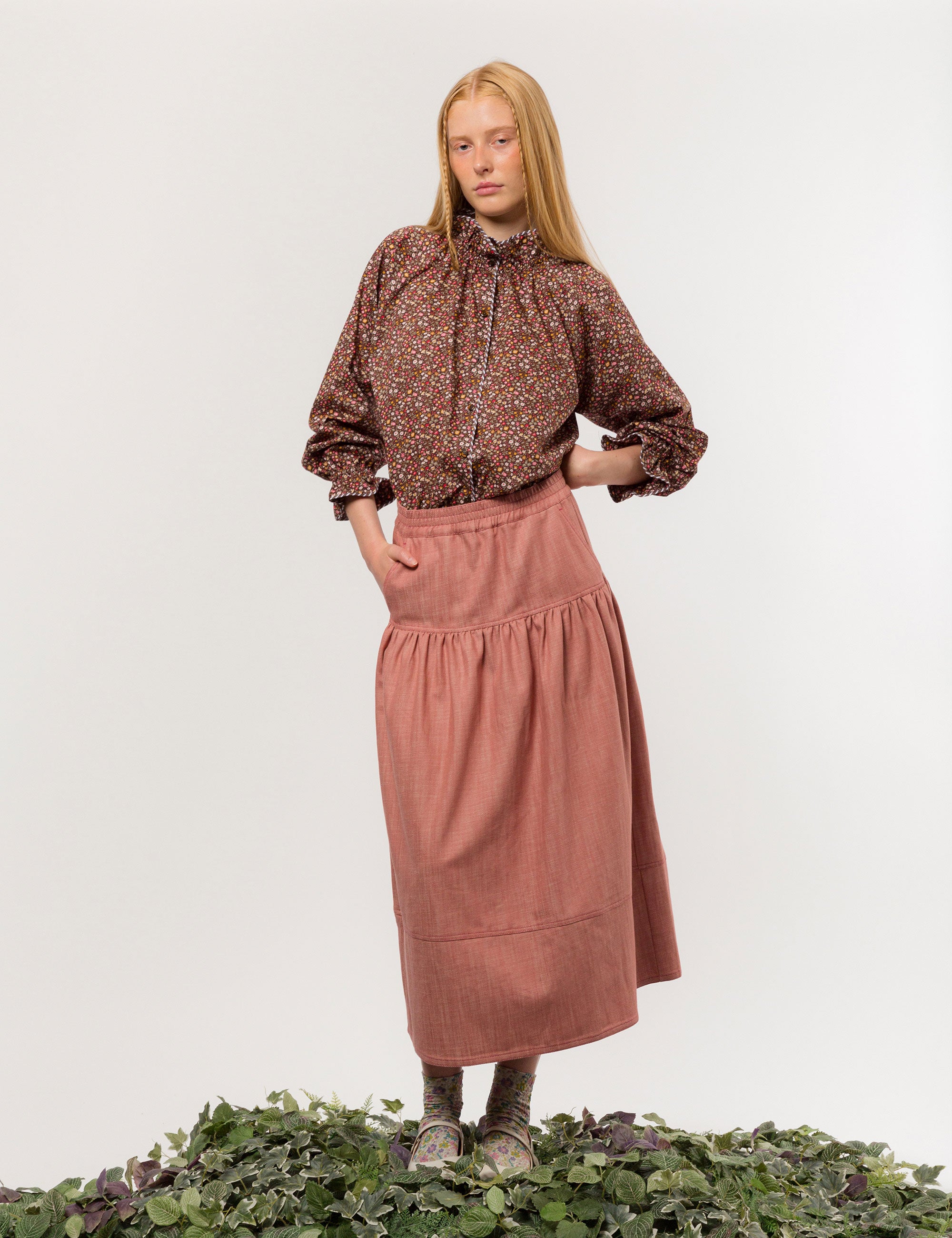 Woman in liberty cotton brown floral print shirt with frilled cuffs and collar and pink cotton skirt