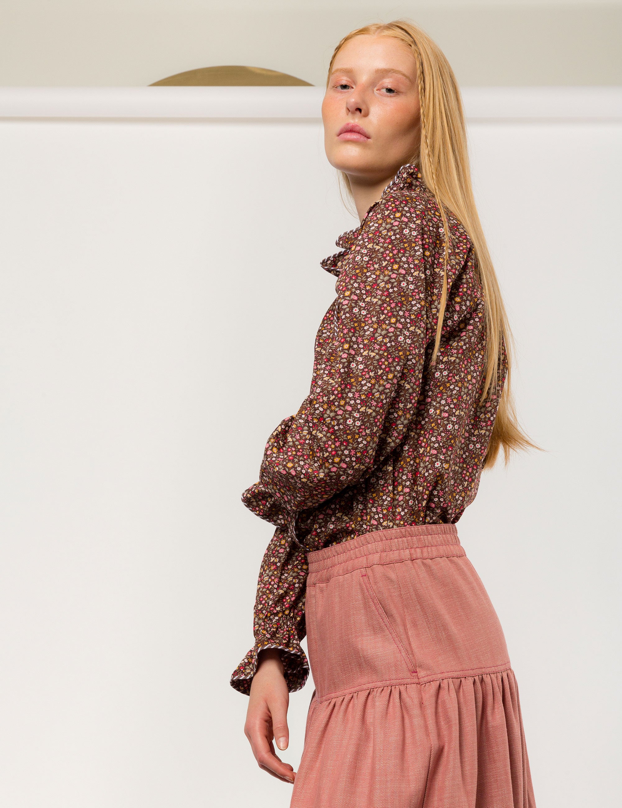 Woman in liberty cotton brown floral print shirt with frilled cuffs and collar and pink cotton skirt