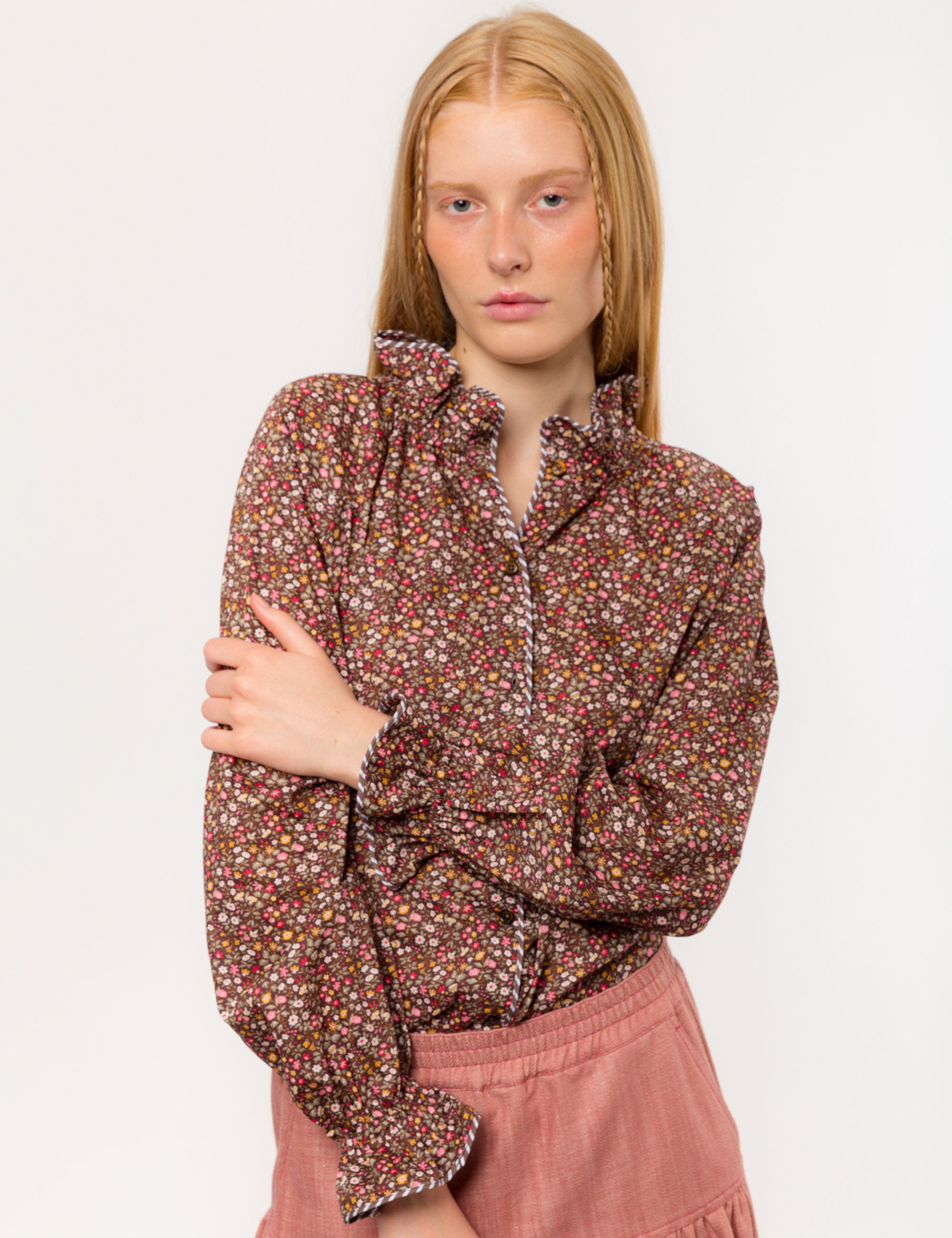 Woman in liberty cotton brown floral print shirt with frilled cuffs and collar and pink cotton skirt