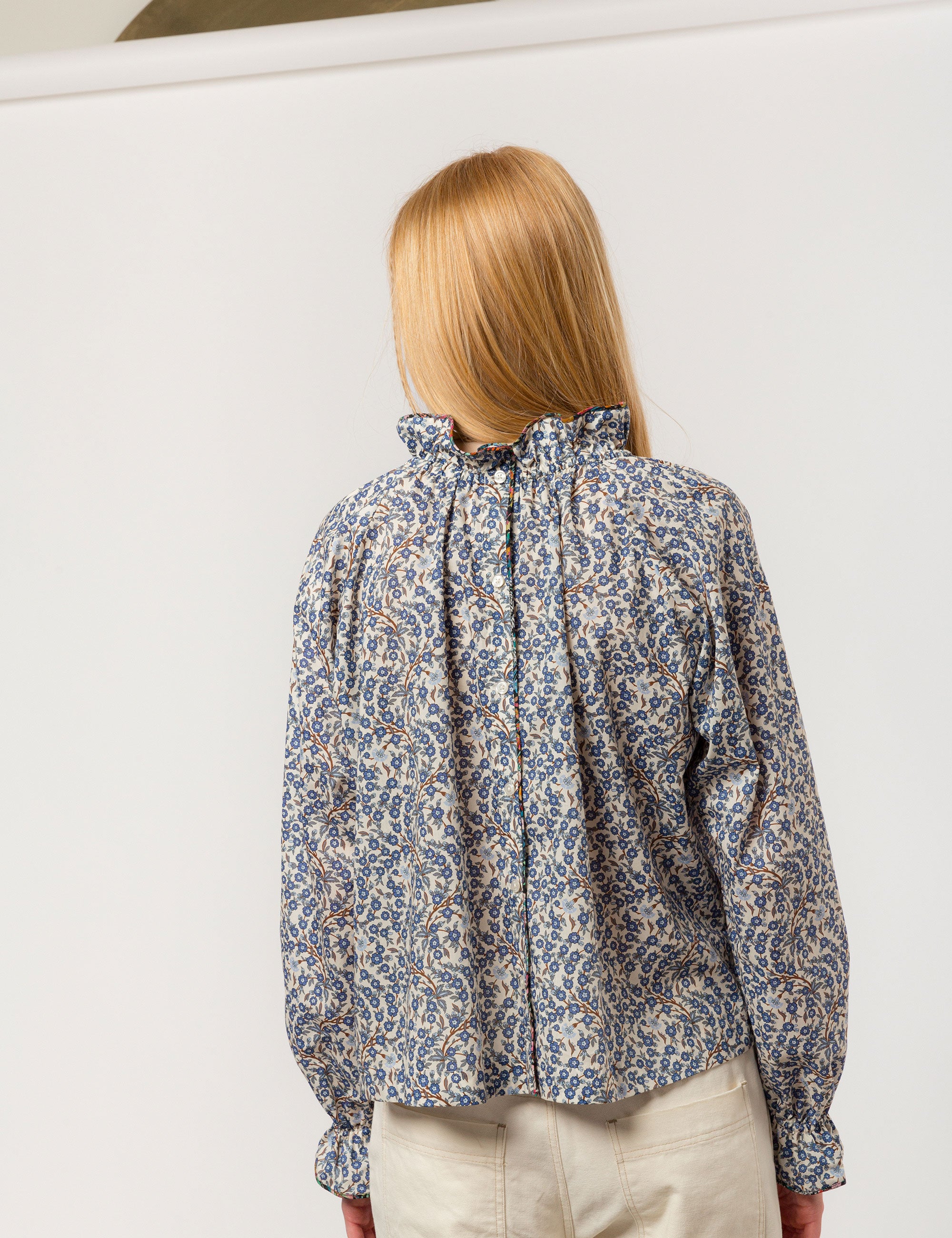 Woman in blue and white floral print liberty cotton shirt with frilled cuffs and collar and creme colored canvas pants