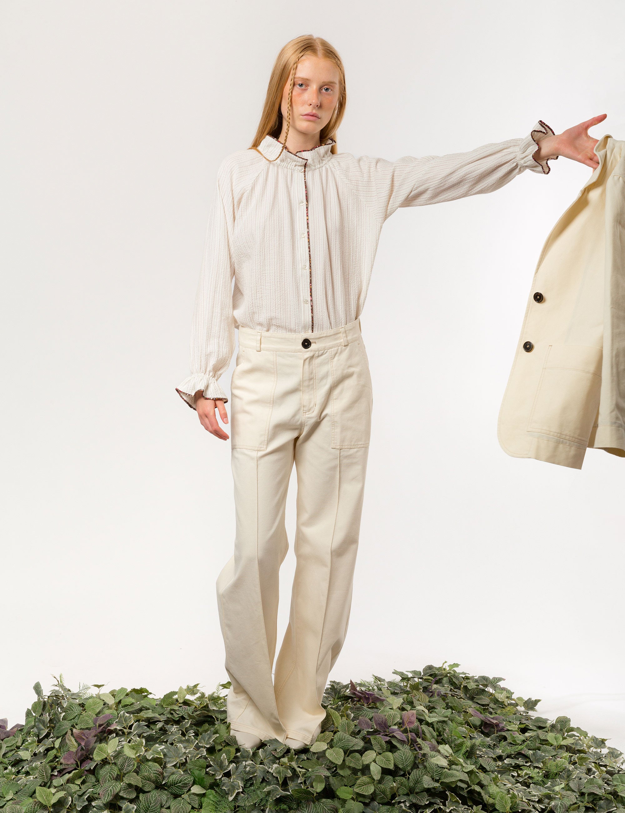 Woman in creme white wide canvas pants and jacket and white long-sleeved  shirt with frilled collar and cuffs
