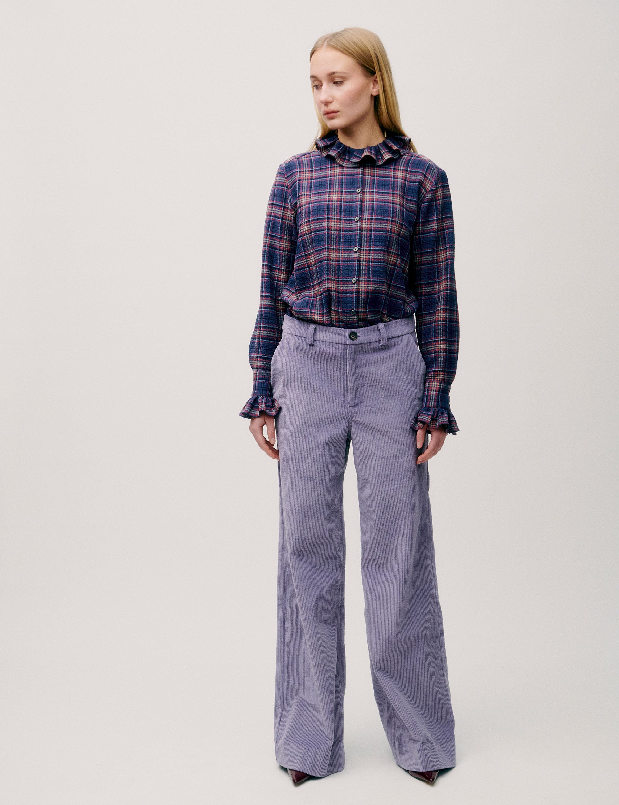 Front view of woman wearing purple wide-leg corduroy trousers and plaid shirt