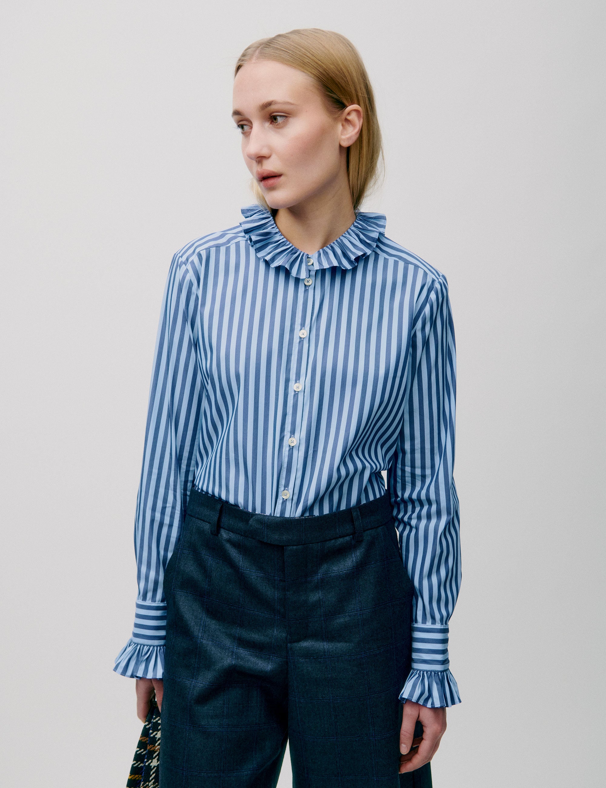 Woman wearing a blue and white striped blouse with ruffle collar and cuffs, paired with dark trousers