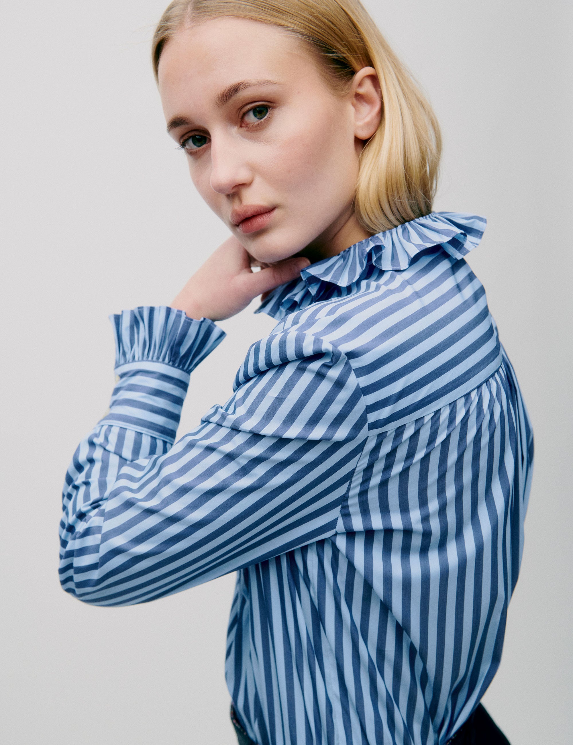 Close-up of ruffle collar and striped sleeve on blue and white blouse