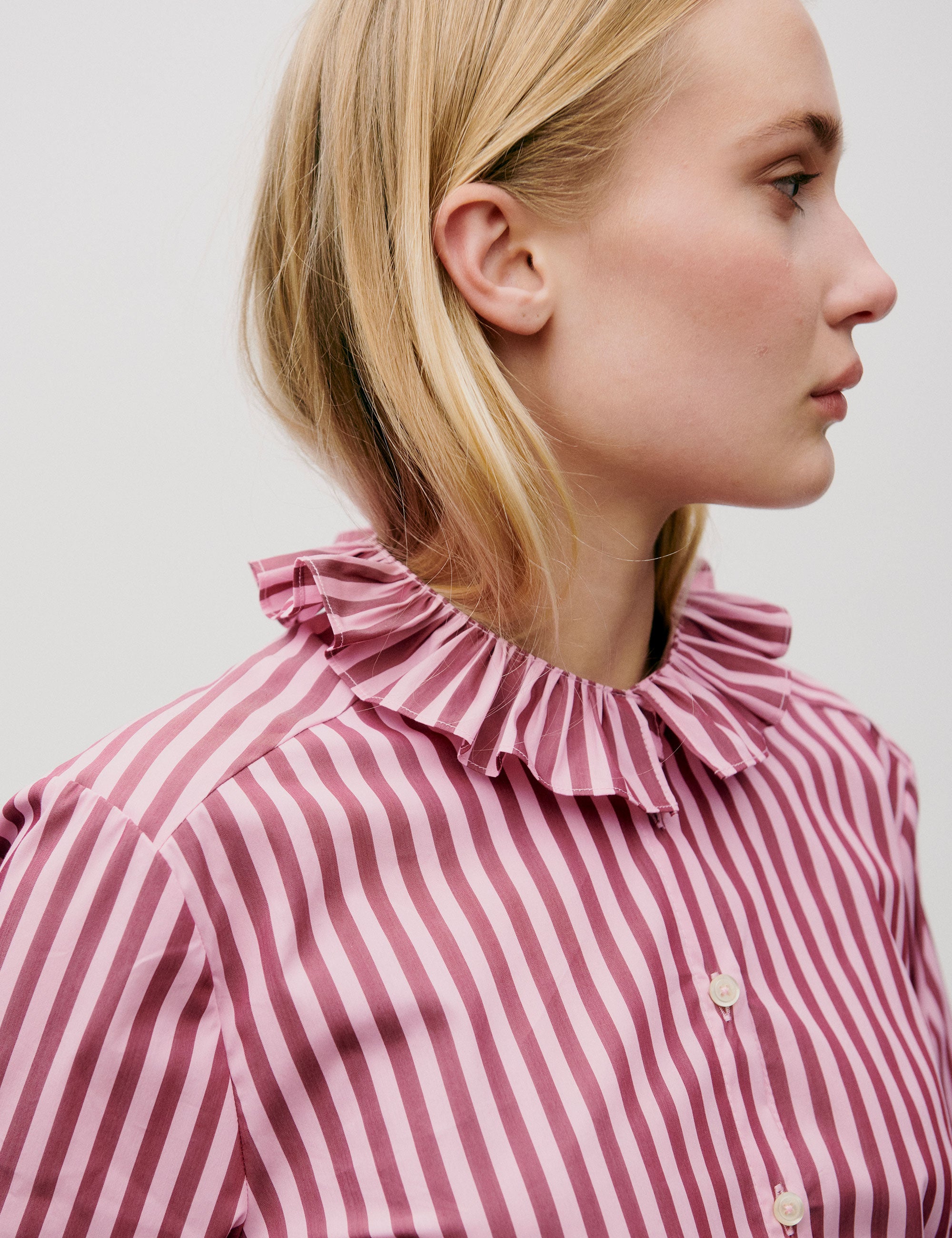 Woman wearing a pink and white striped shirt with a ruffled collar against a plain background