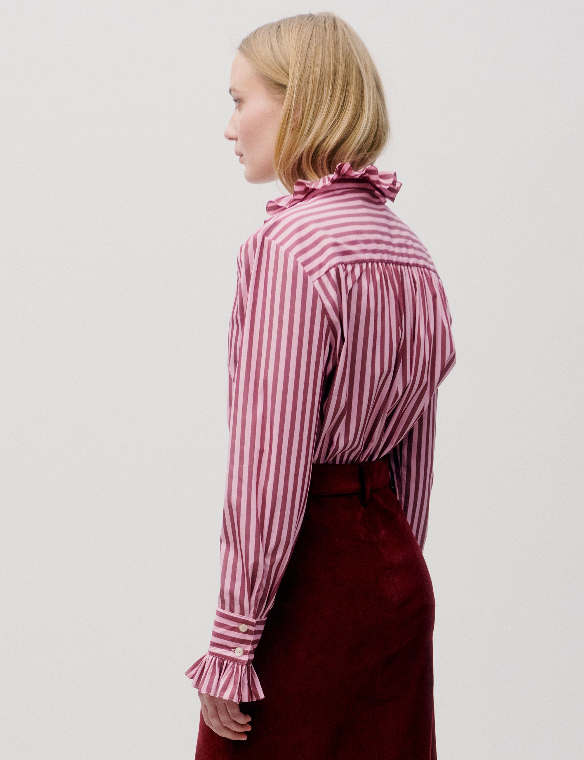 Woman wearing a pink and white striped blouse with a high collar and long sleeves.