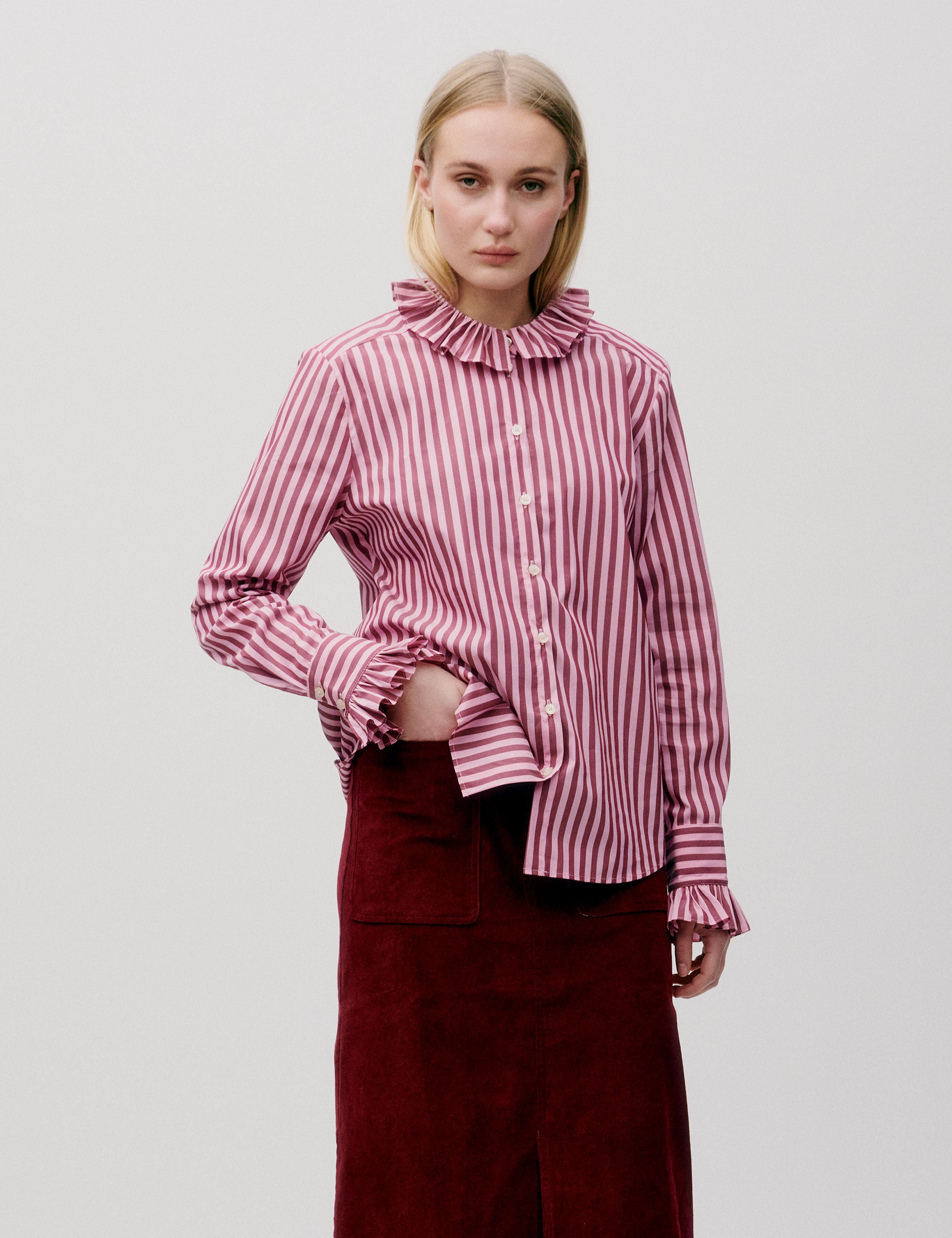 Woman wearing a red and white striped shirt with a high collar on a plain background