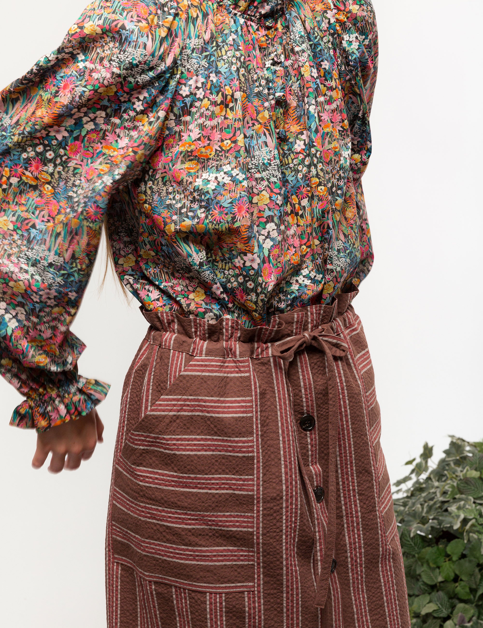 Woman in liberty cotton multi-colored floral print shirt with frilled cuffs and collar and brown striped skirt