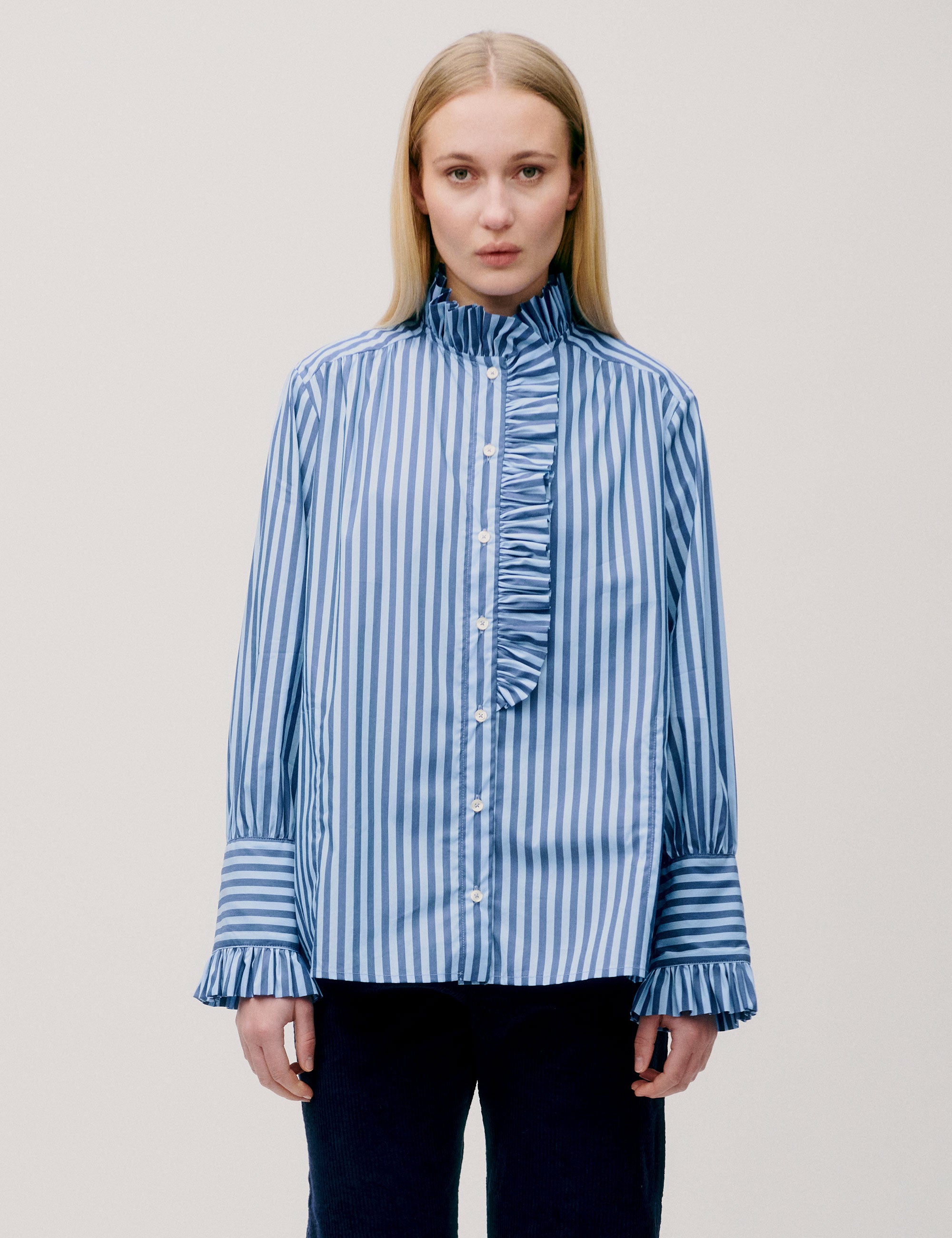 Front view of woman wearing blue striped blouse with ruffle collar and cuffs