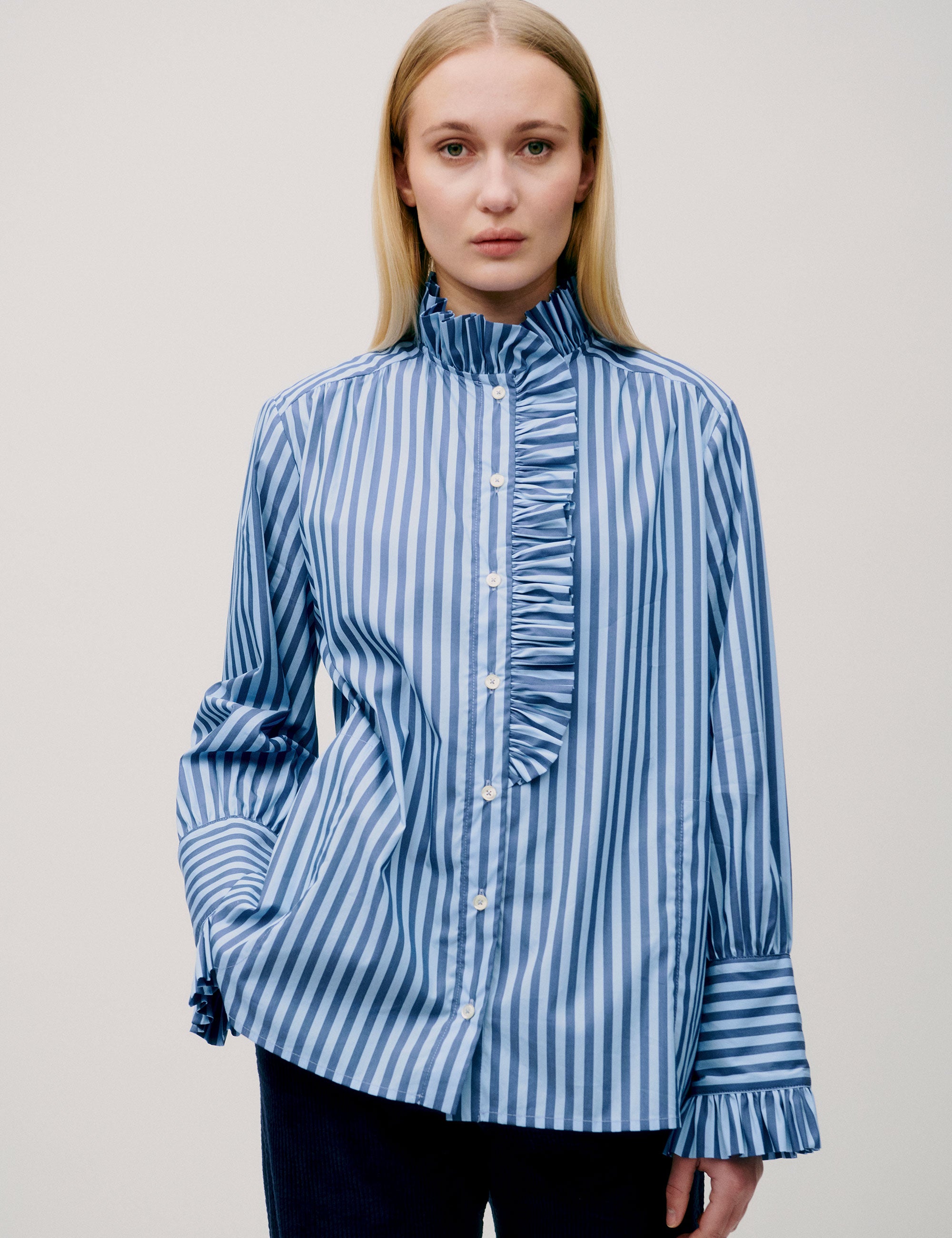 Woman in blue striped blouse with hands in pockets, front view