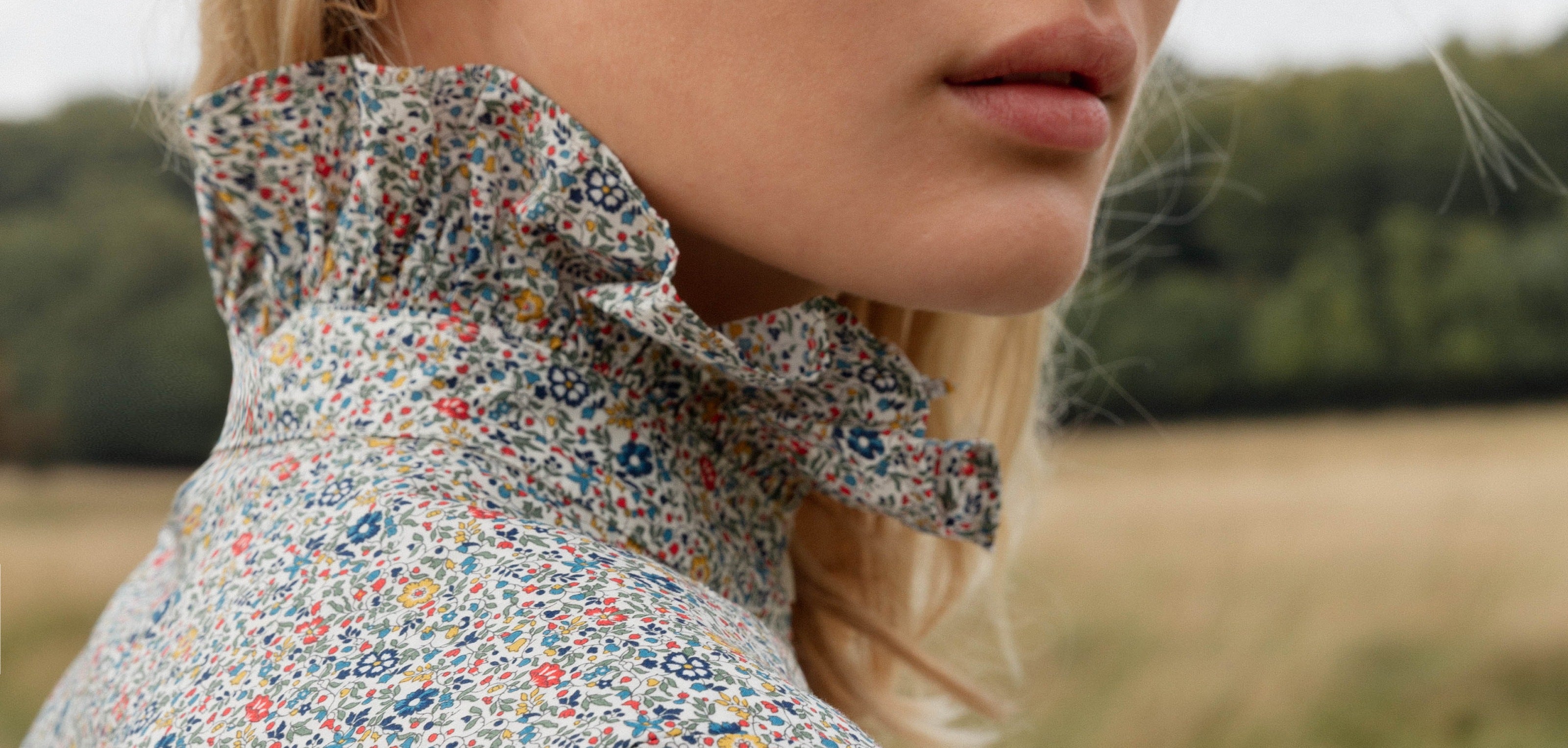 Close-up of a woman wearing an APOF  floral blouse with ruffled collar on a blurred natural background