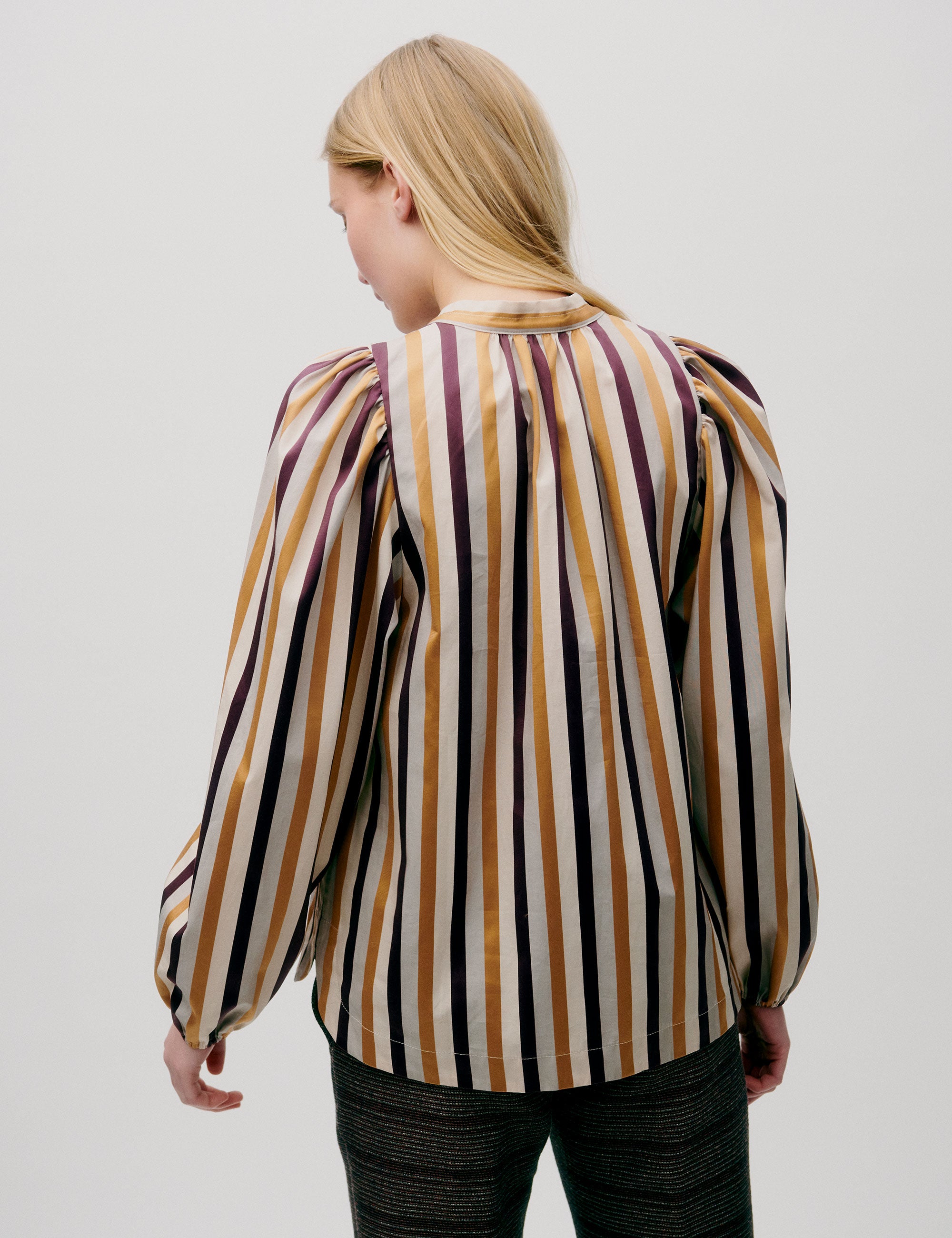 Woman wearing loose-fit striped blouse in mustard, burgundy, and cream tones