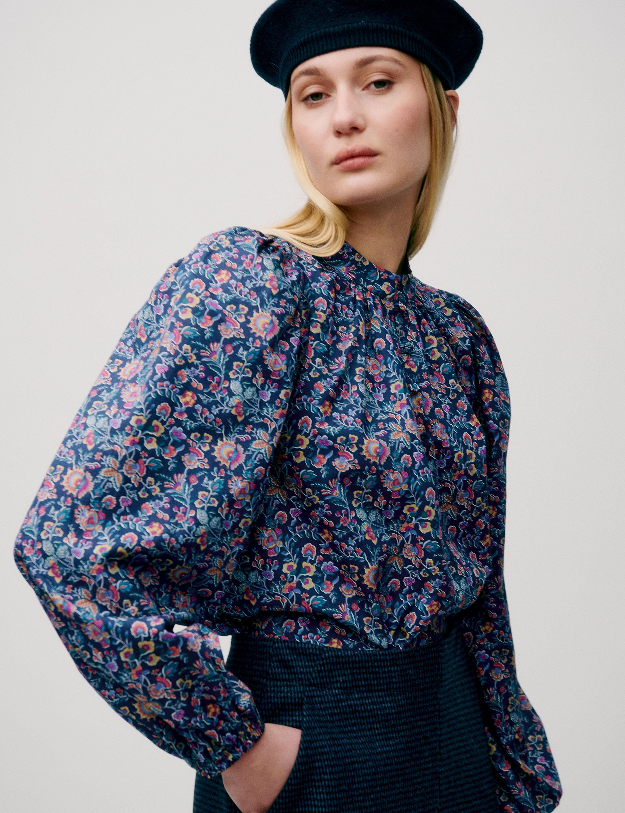 Woman wearing a floral blouse with balloon sleeves and a dark blue skirt, styled with a beret
