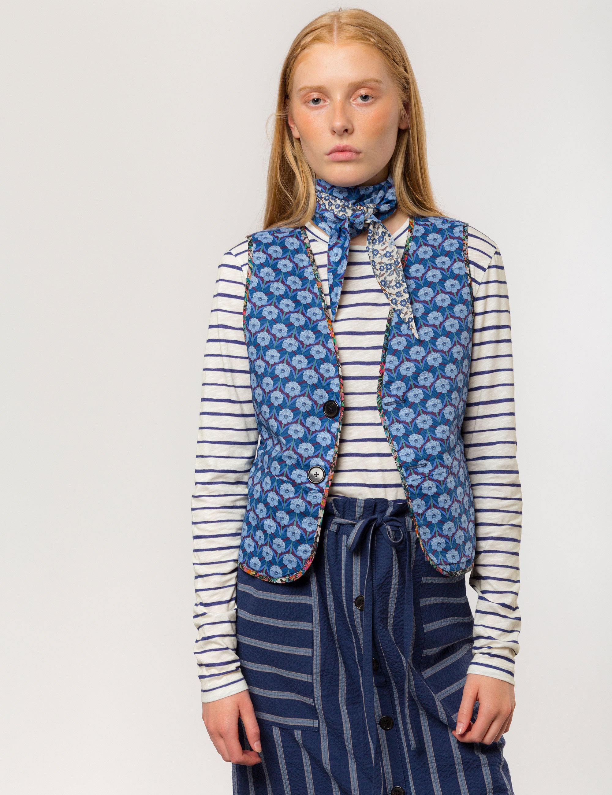 Woman in long sleeved white and blue striped cotton jersey t-shirt, blue and white striped skirt and blue flower patterned vest