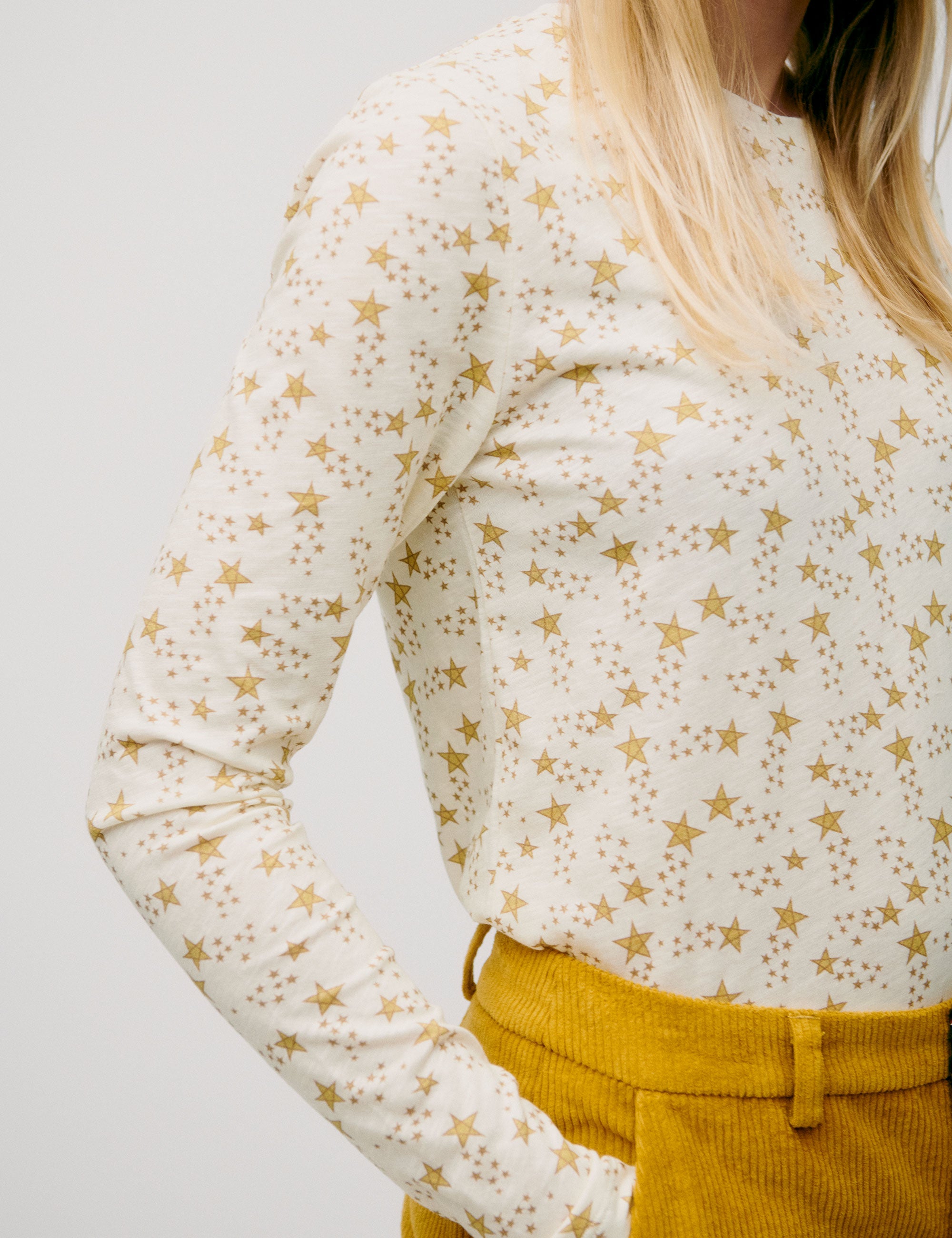Woman wearing a cream long-sleeve top with gold star print, paired with mustard yellow corduroy trousers