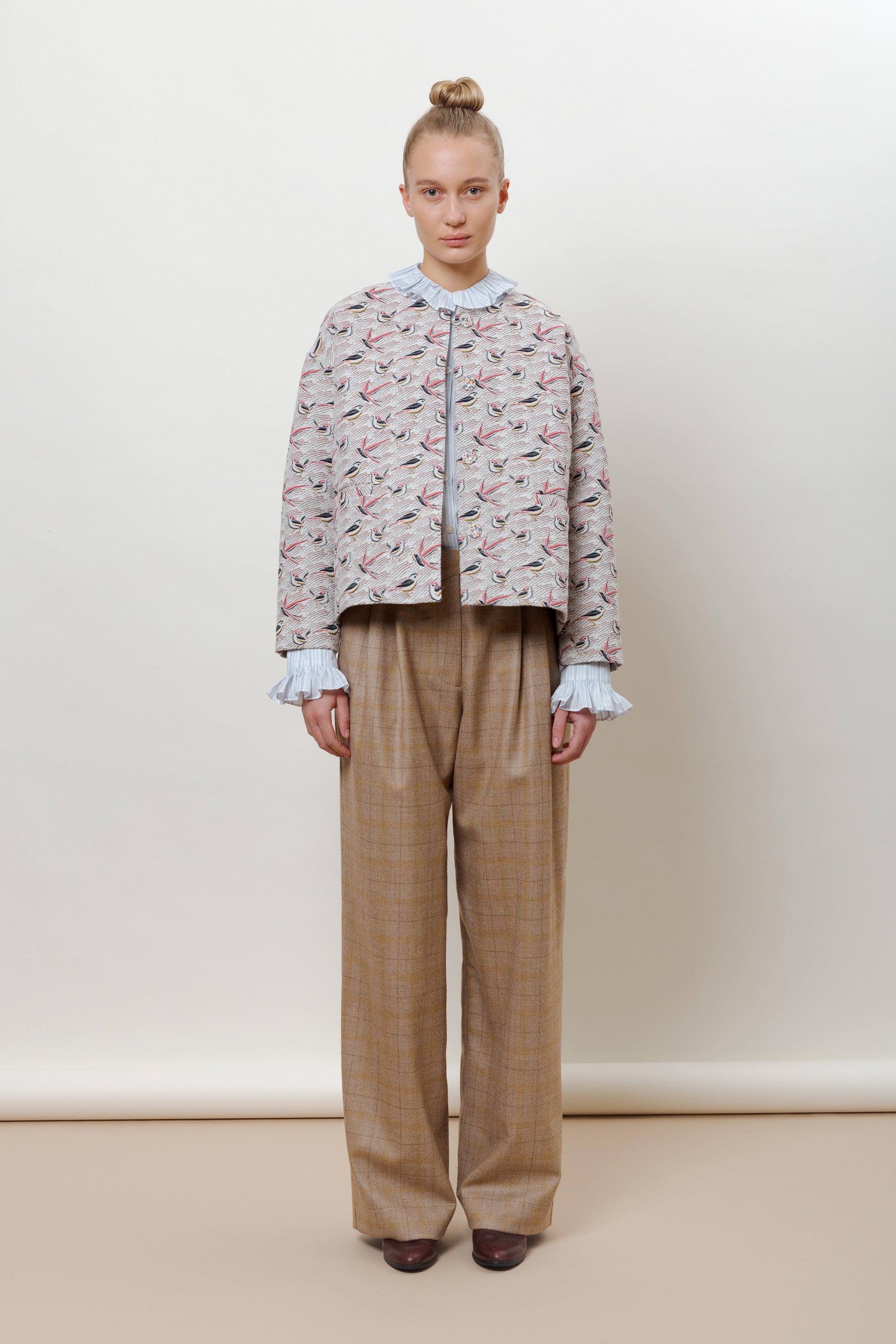 Woman in jacket with bird pattern, frilled blouse and brown pants