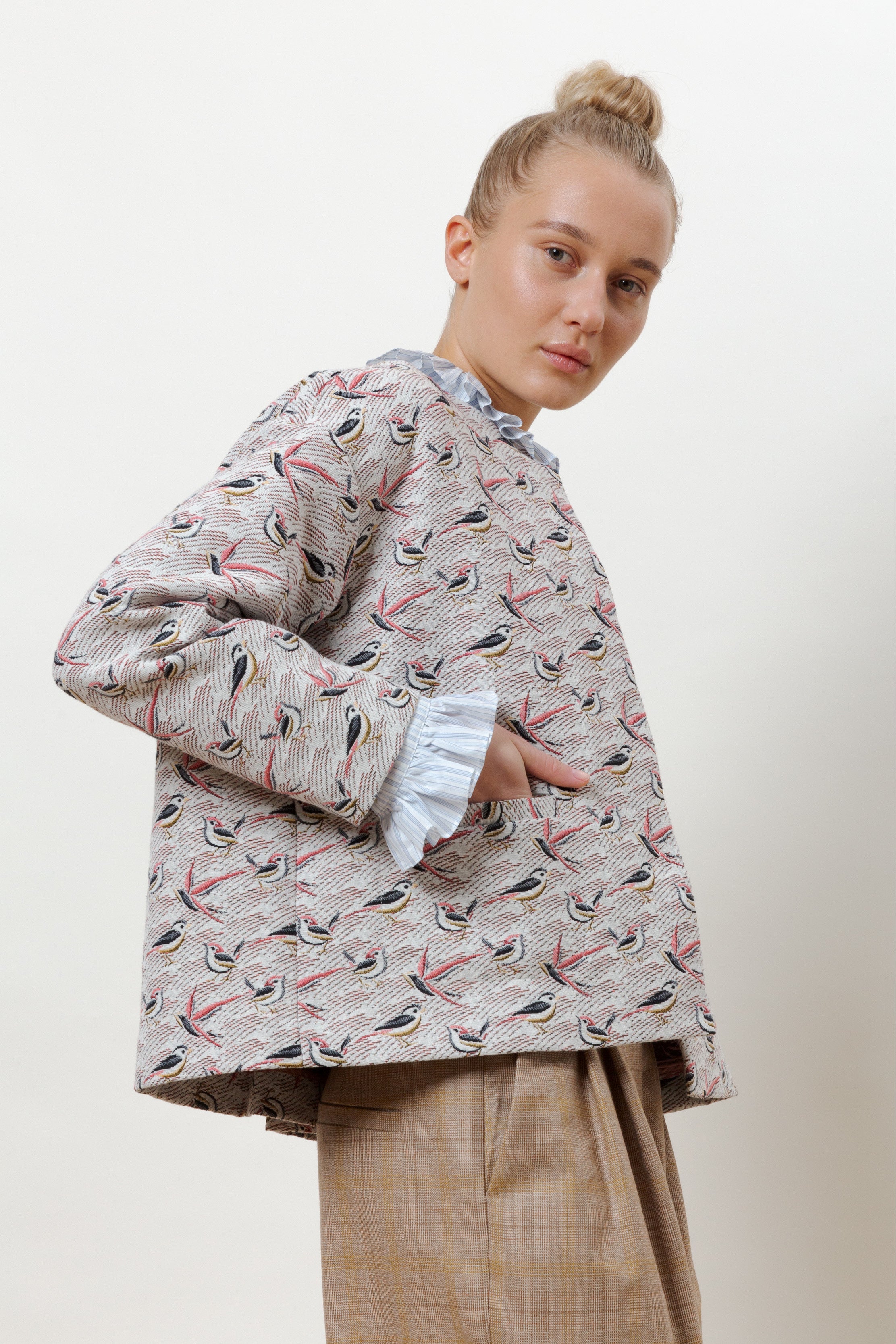 Woman in jacket with bird pattern, frilled blouse and brown pants