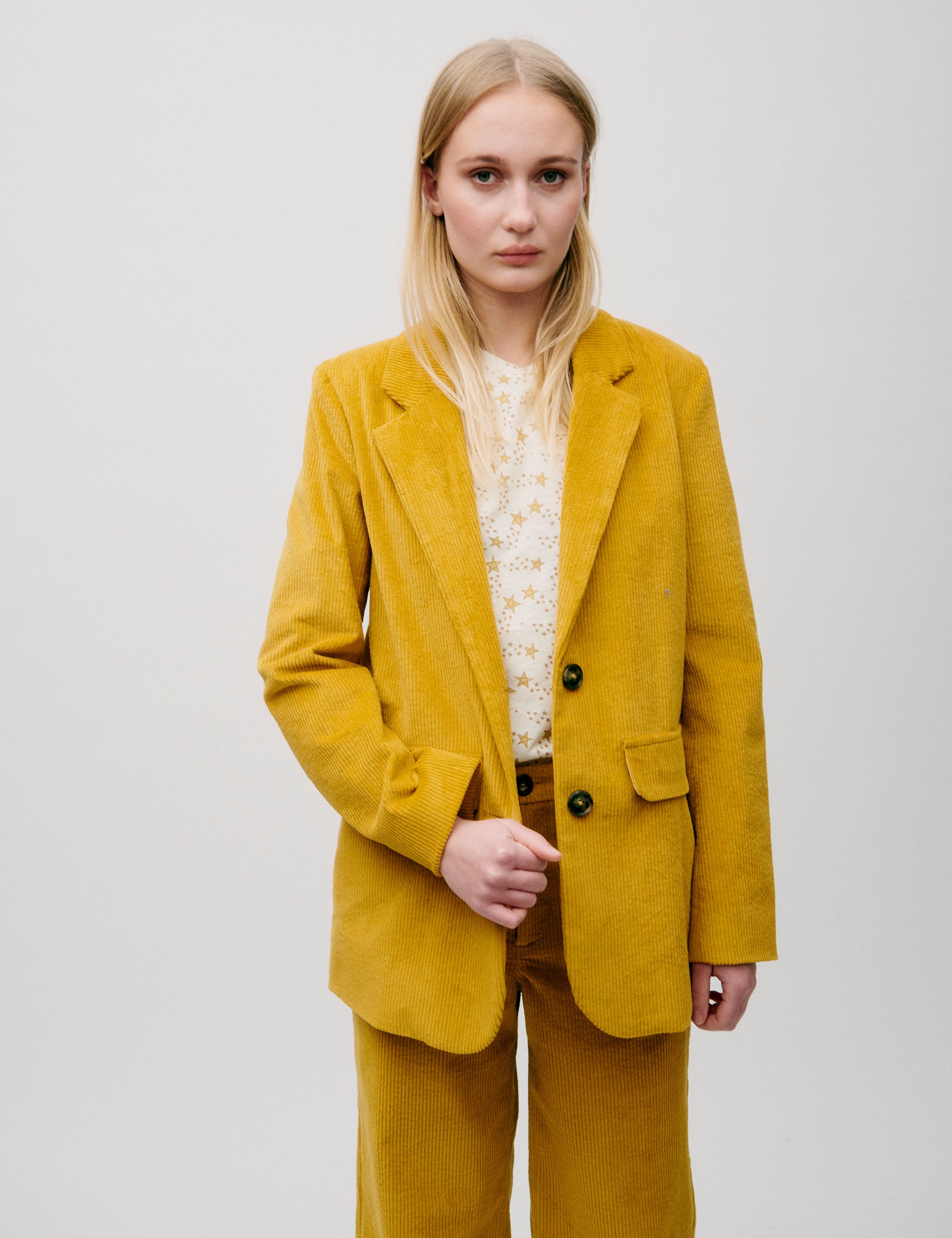 Woman wearing a mustard yellow corduroy blazer with two-button closure, styled with matching trousers and a cream printed t-shirt