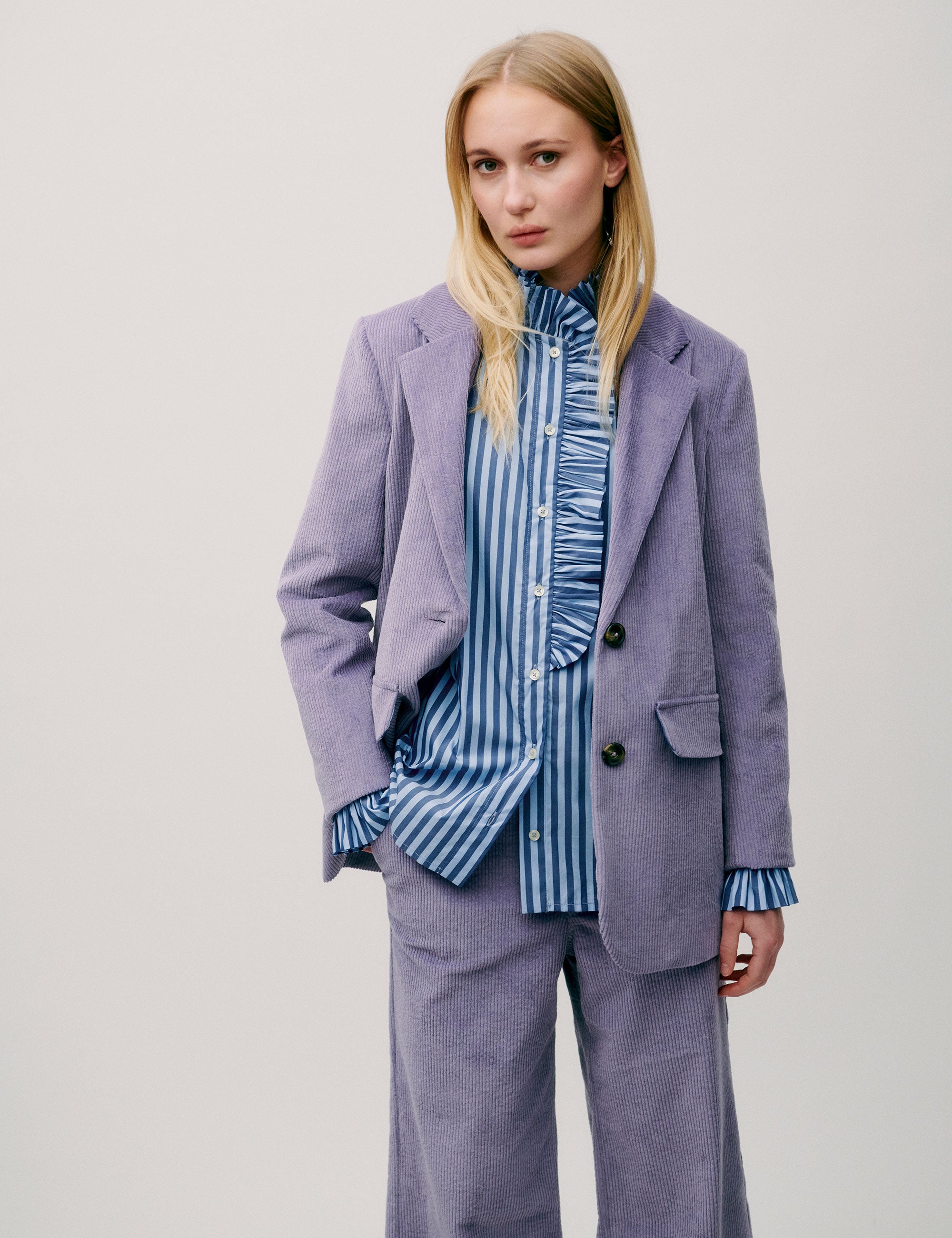 Woman wearing a lilac corduroy blazer with two-button closure and flap pockets, styled over a blue striped blouse