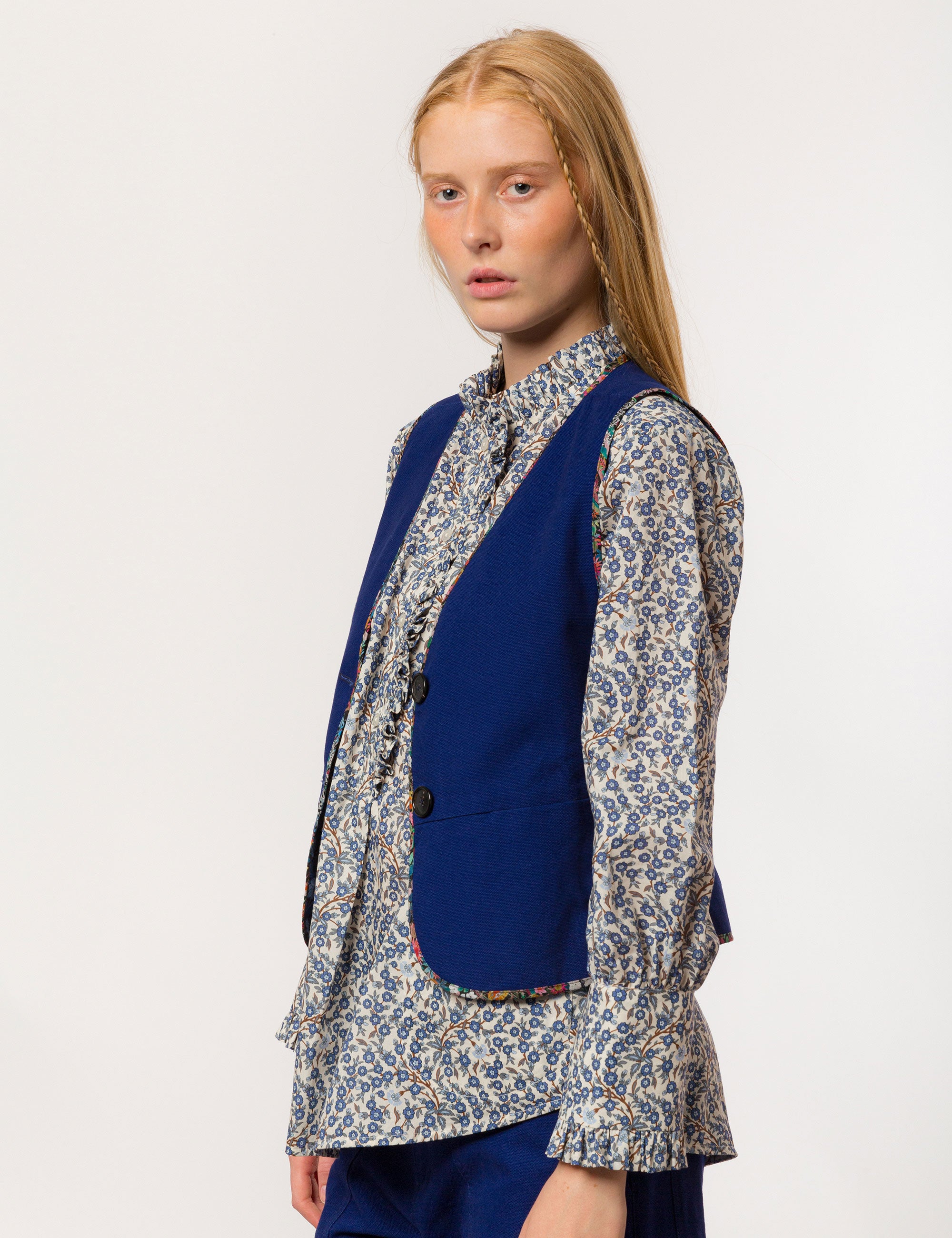 Woman in long sleeved white and blue floral print shirt, blue vest and pants