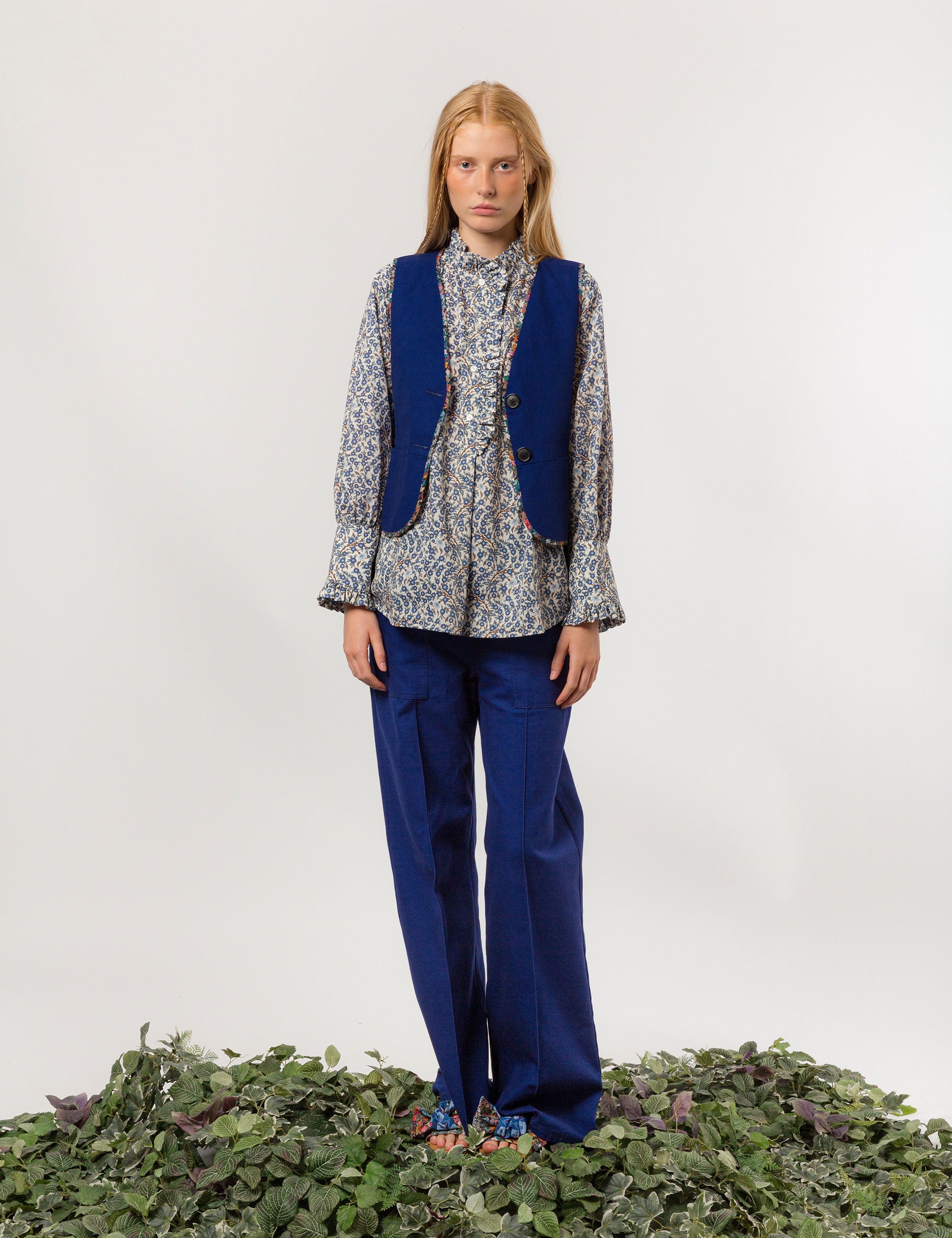 Woman in long sleeved white and blue floral print shirt, indigo blue canvas vest and wide cut canvas pants