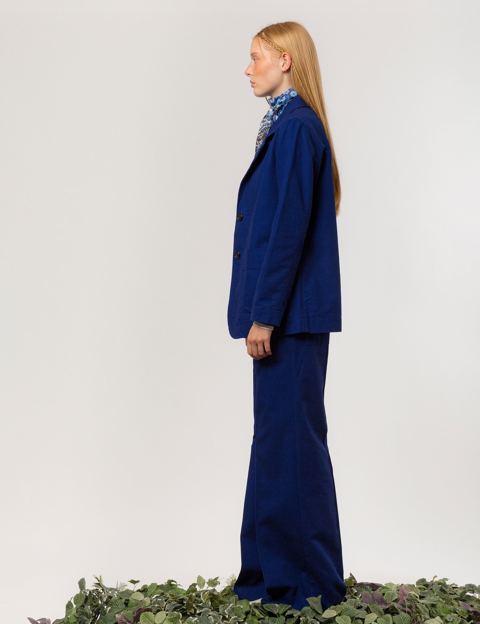 Woman in indigo blue canvas jacket blazer with buttons and pockets, matching wide canvas trousers and flower patterned bandana around neck