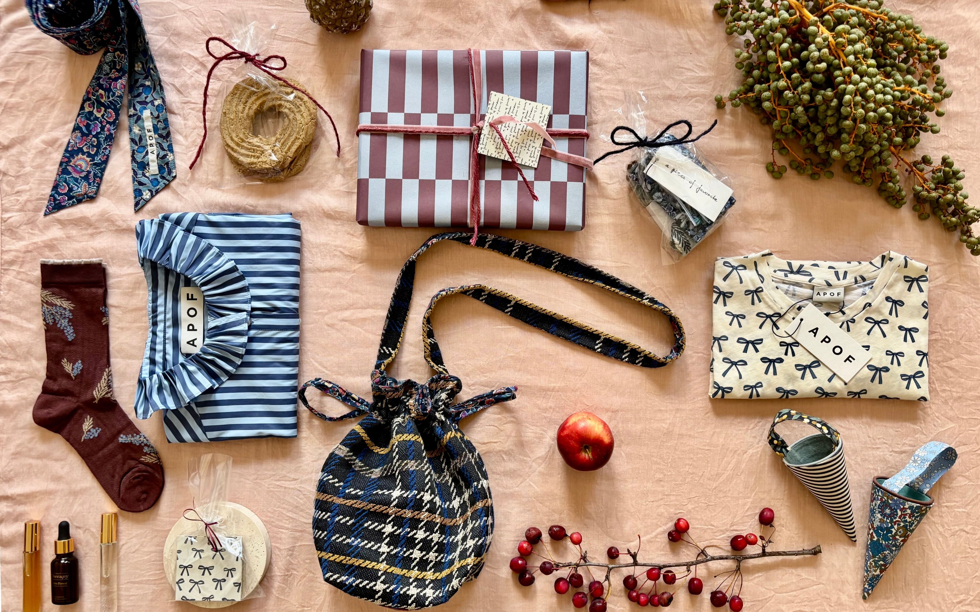 Julegaver og accessories fra APOF lagt på bord – skjorter, strømper, tasker og indpakkede pakker i varme farver.
