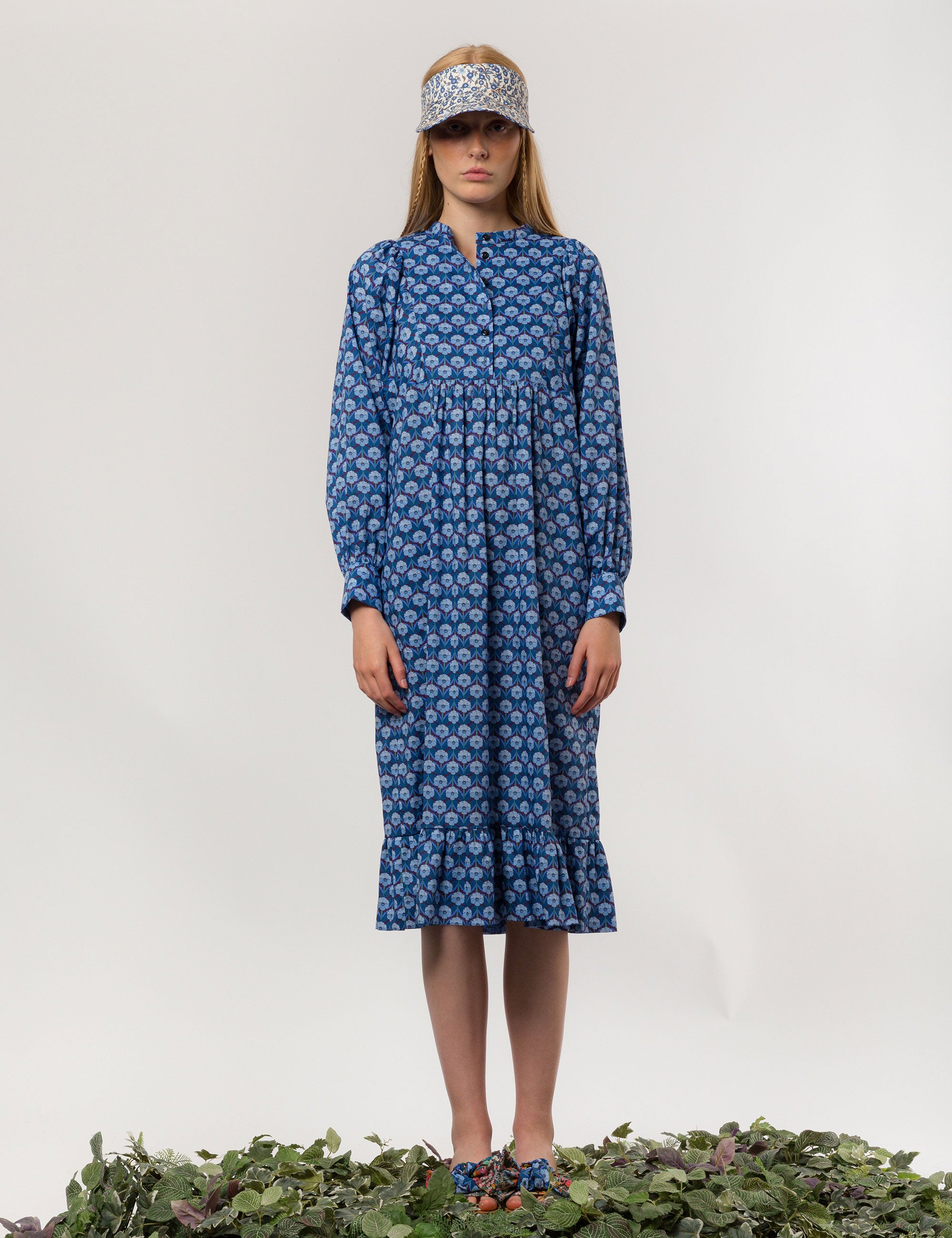 Woman in blue floral patterned dress with long sleeves and sun shade cap with blue and white flower pattern