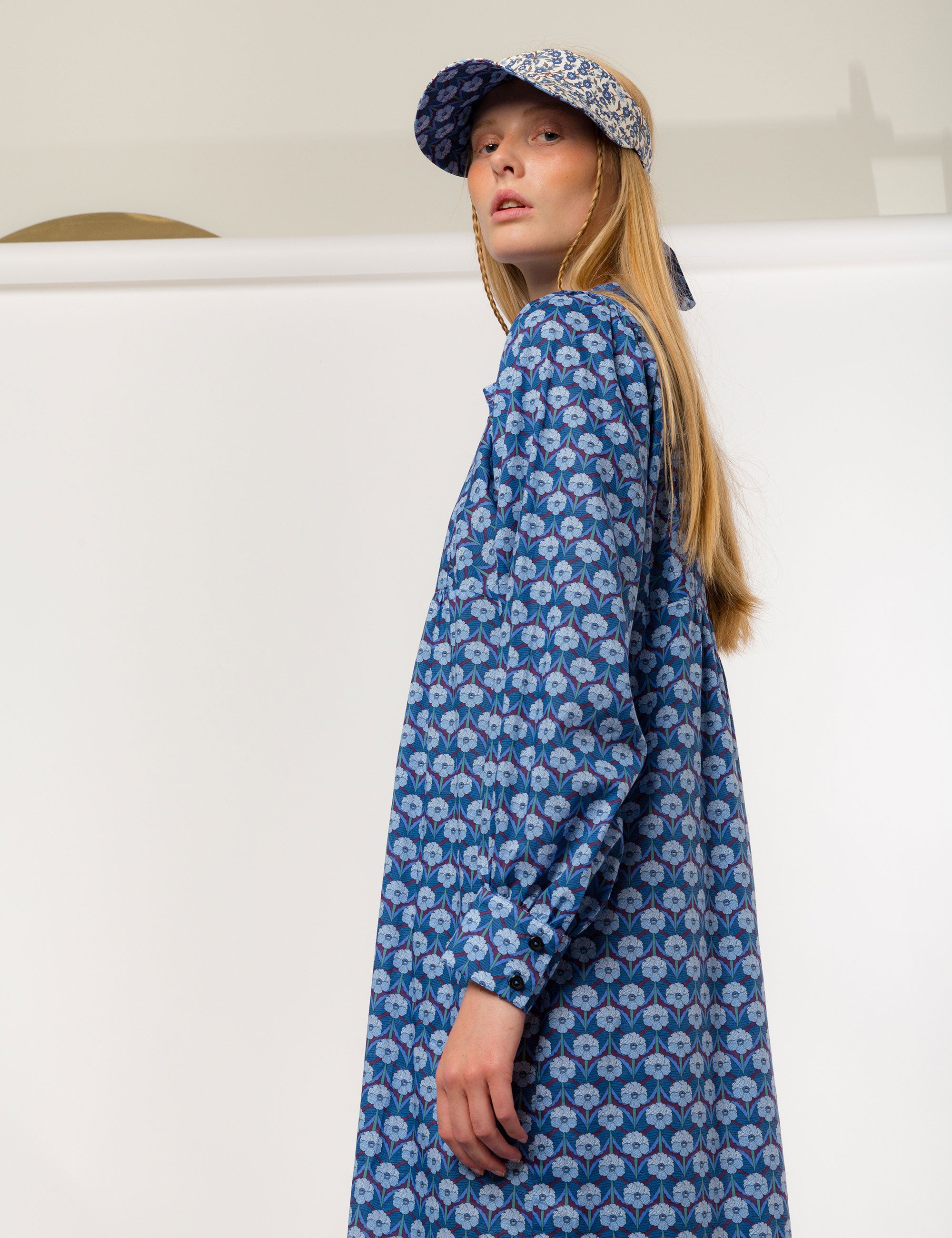 Woman in blue floral patterned dress with long sleeves and sun shade cap with blue and white flower pattern