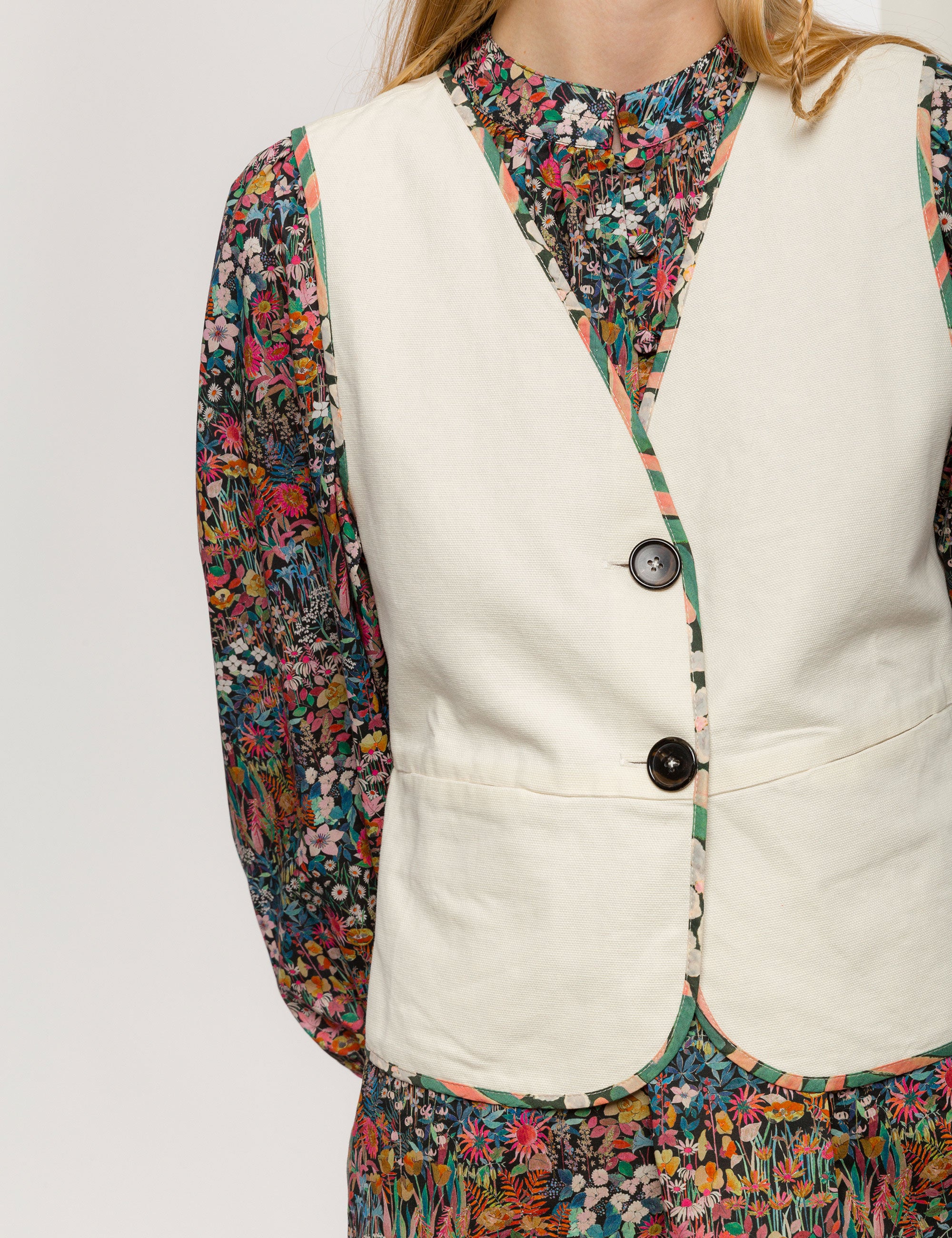 Woman in reversible cream colored vest with buttons, pockets and floral print pipings and multi-colored floral dress