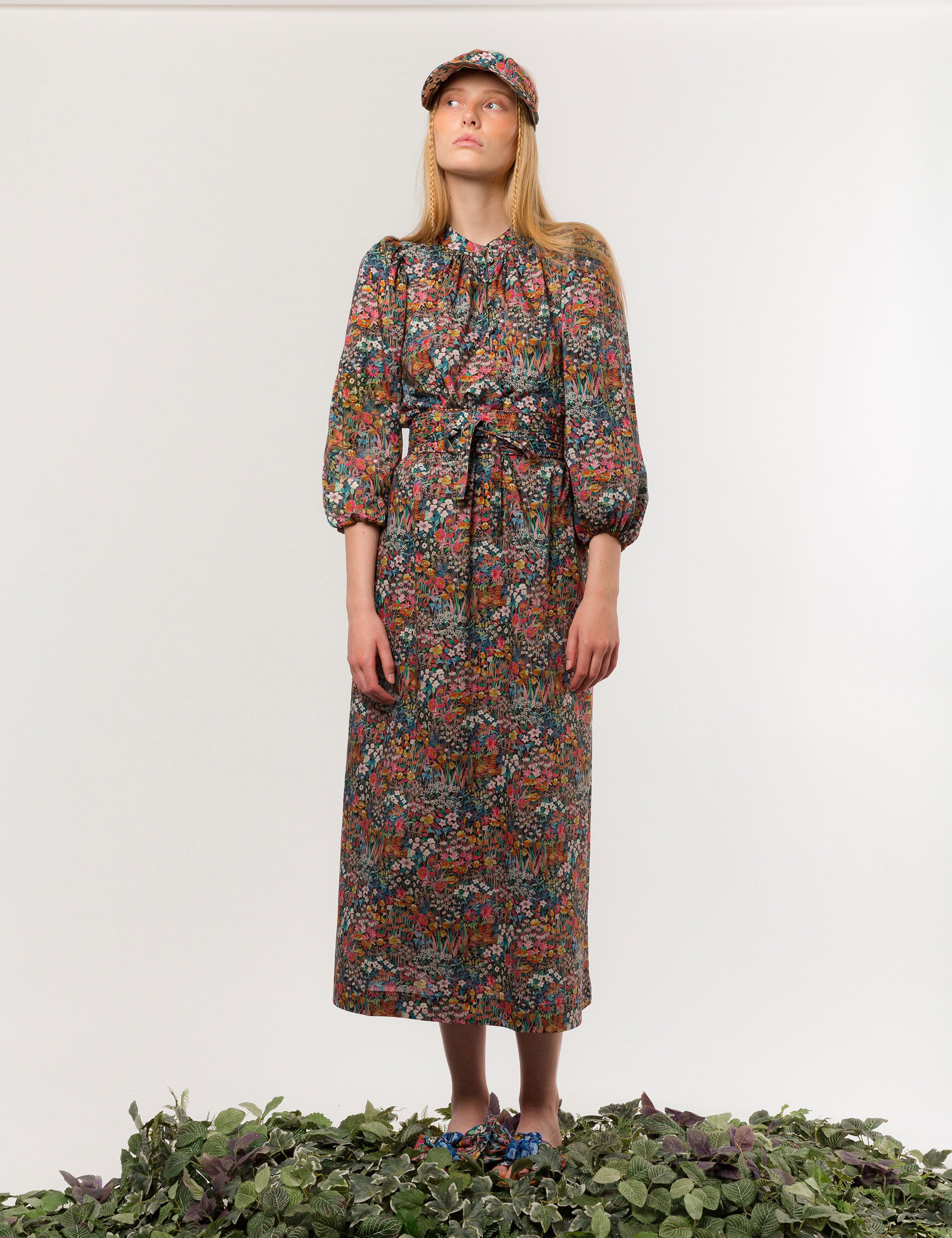 Woman in multicolored floral patterned dress with long sleeves and sun shade cap with multicolored flower pattern