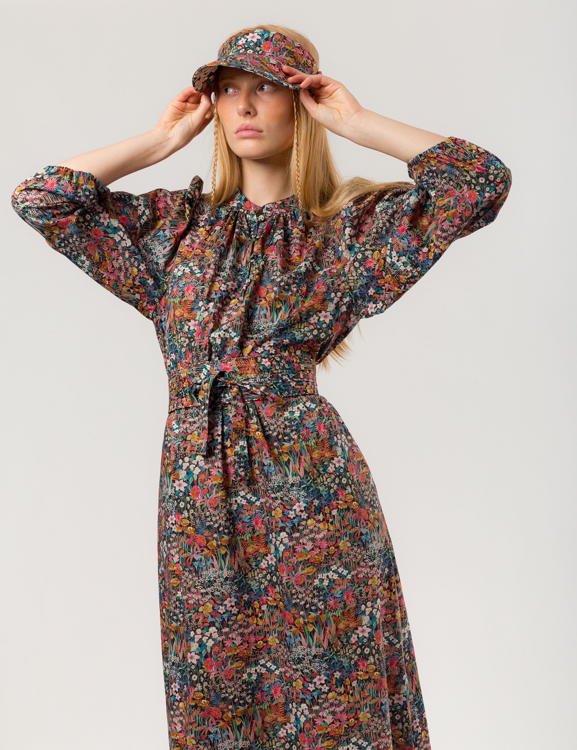 Woman in multicolored floral patterned dress with long sleeves and sun shade cap with multicolored flower pattern