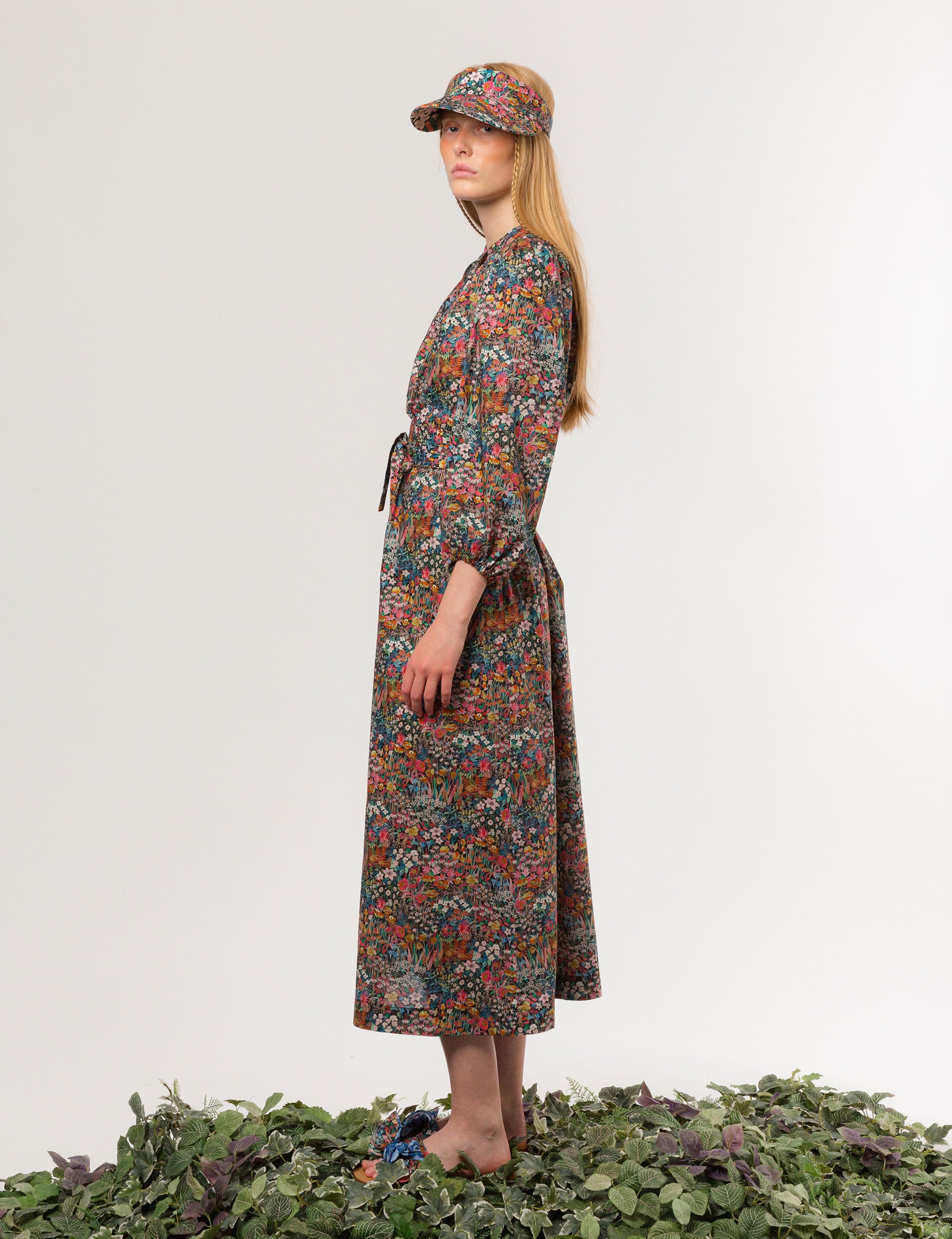 Woman in multicolored floral patterned dress with long sleeves and sun shade cap with multicolored flower pattern