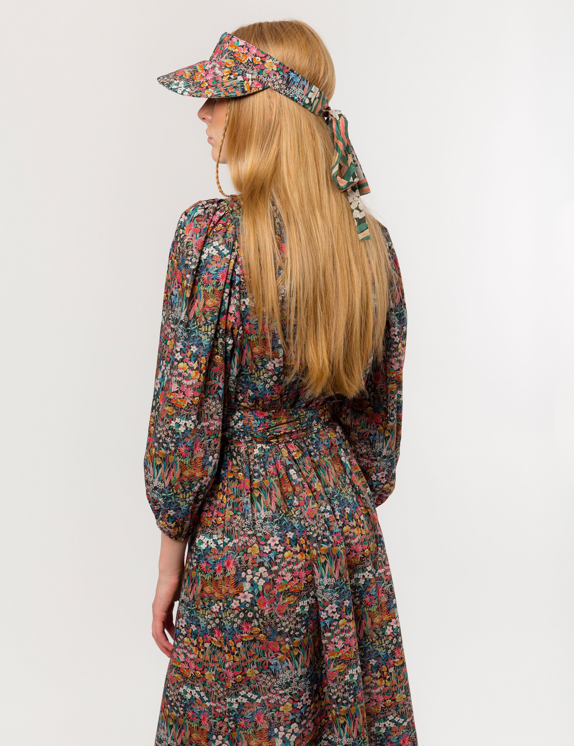 Woman in multicolored floral patterned dress with long sleeves and sun shade cap with multicolored flower pattern