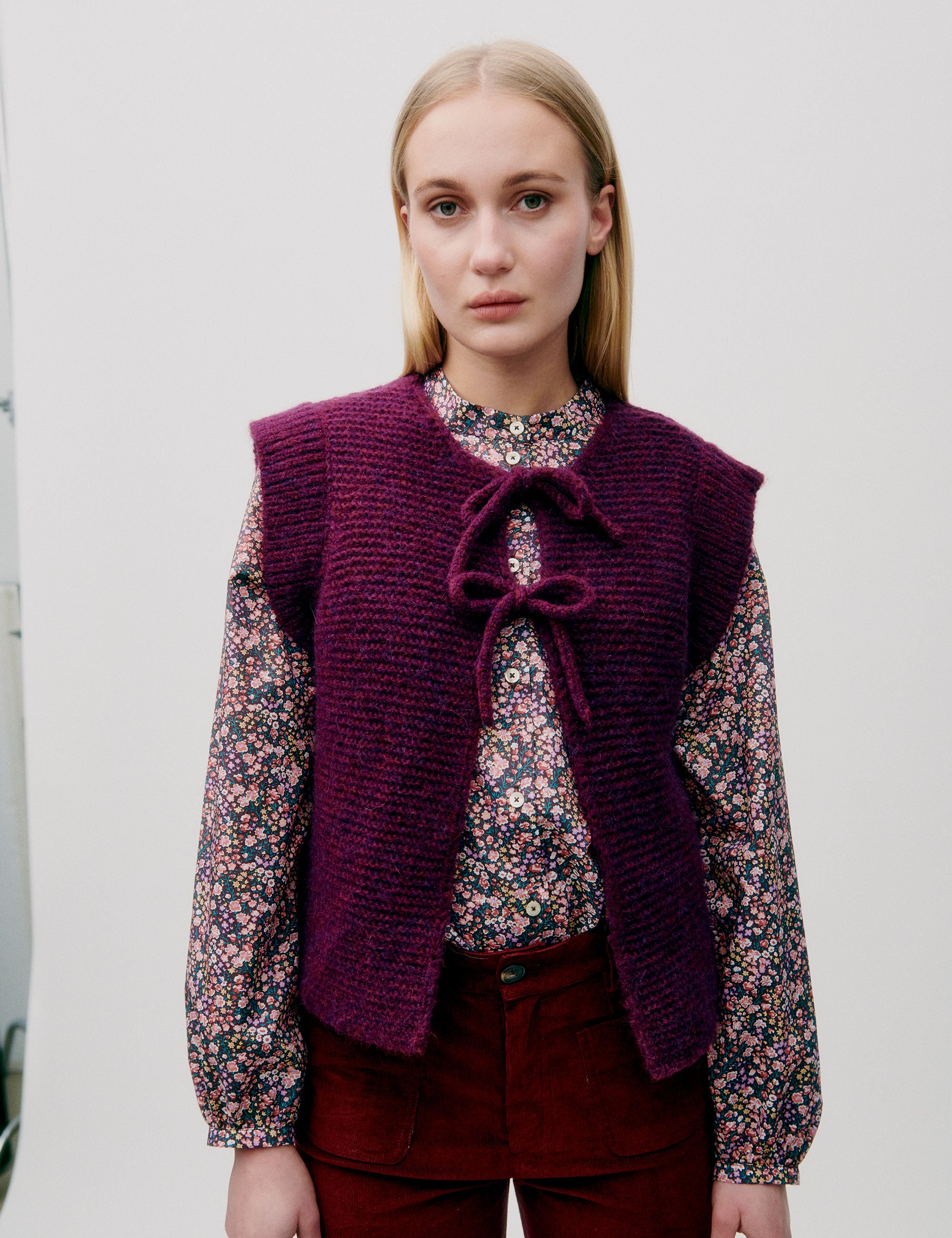 Woman in pink and blue flower patterned shirt with long sleeves and dark pink knitted wool vest