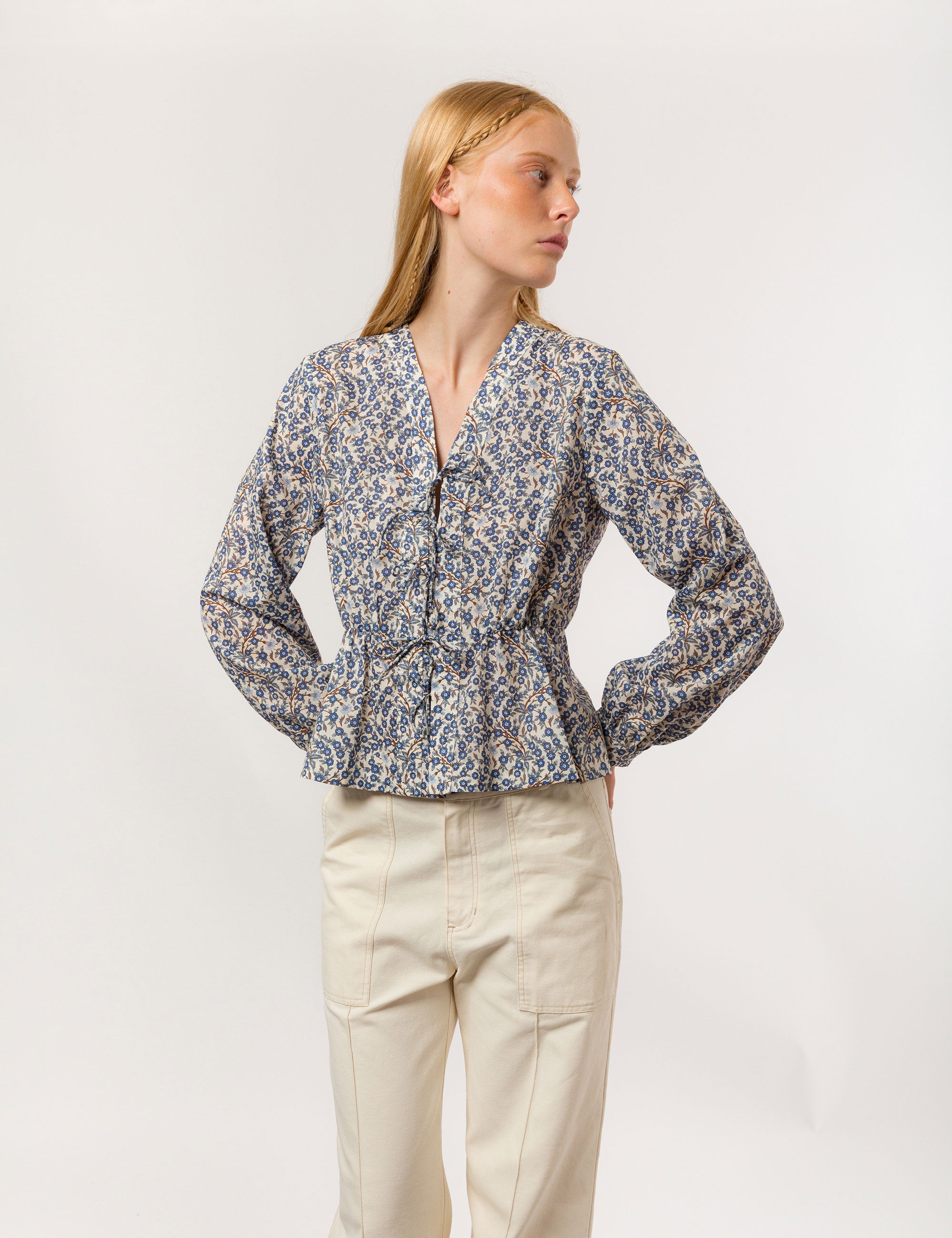 Woman in liberty cotton blue and white floral print blouse with v-neck and long sleeves with cuffs and creme white canvas pants with pockets