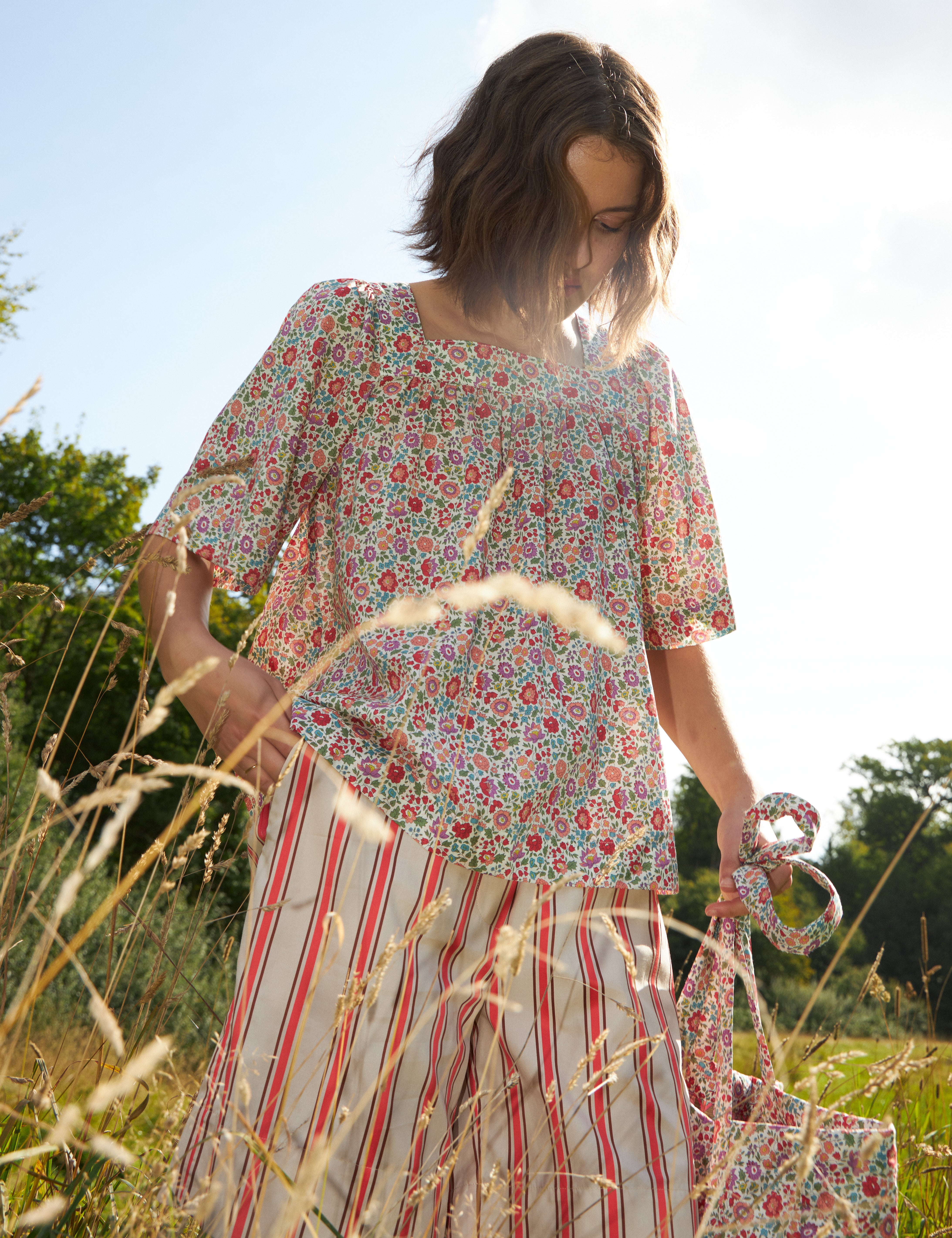 Woman in red and white striped pants and loose fit blouse with short wide sleeves in multi-colored floral patterned Liberty cotton