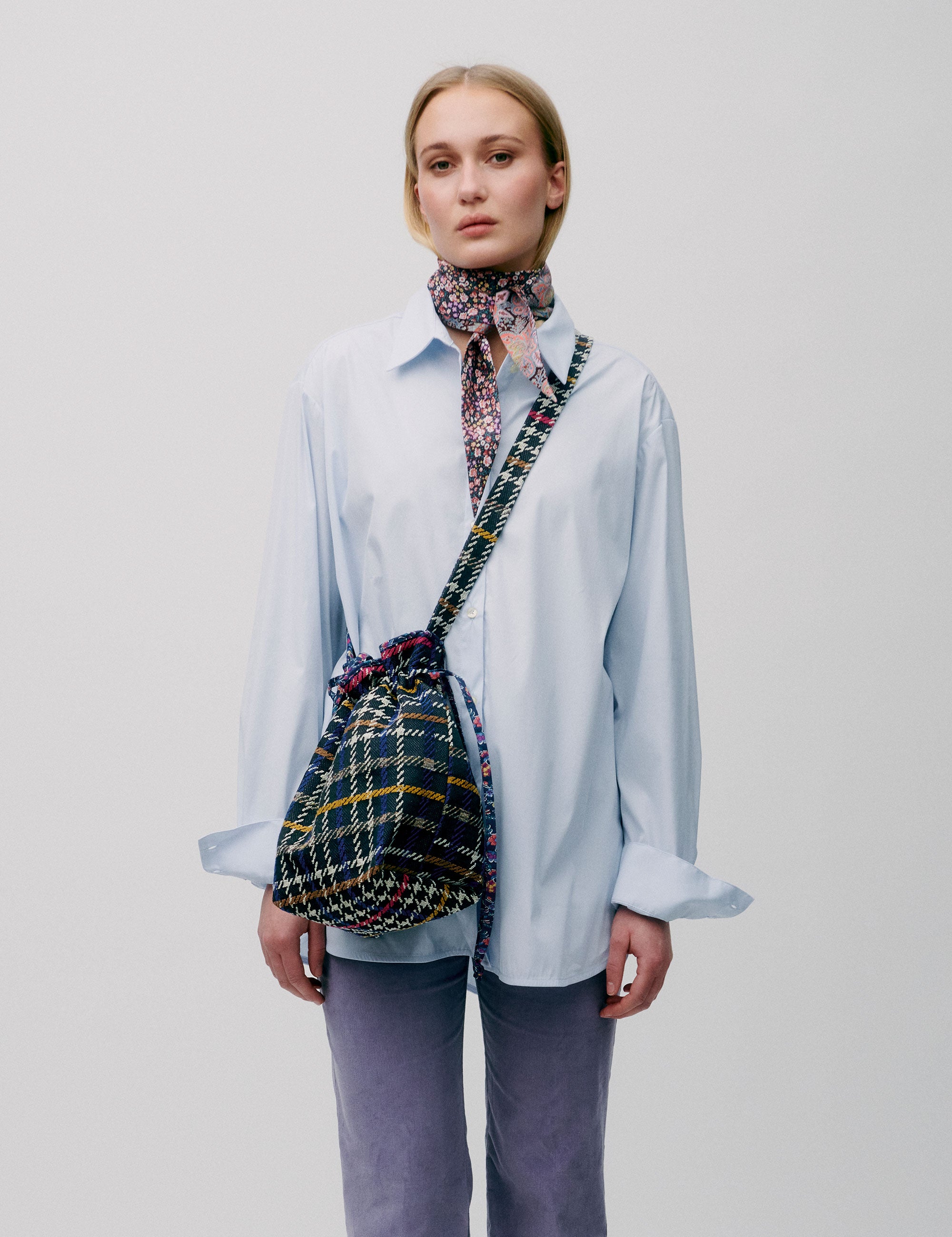 Woman in light blue straight cotton shirt with long sleeves carrying a check patterned crossbody bag