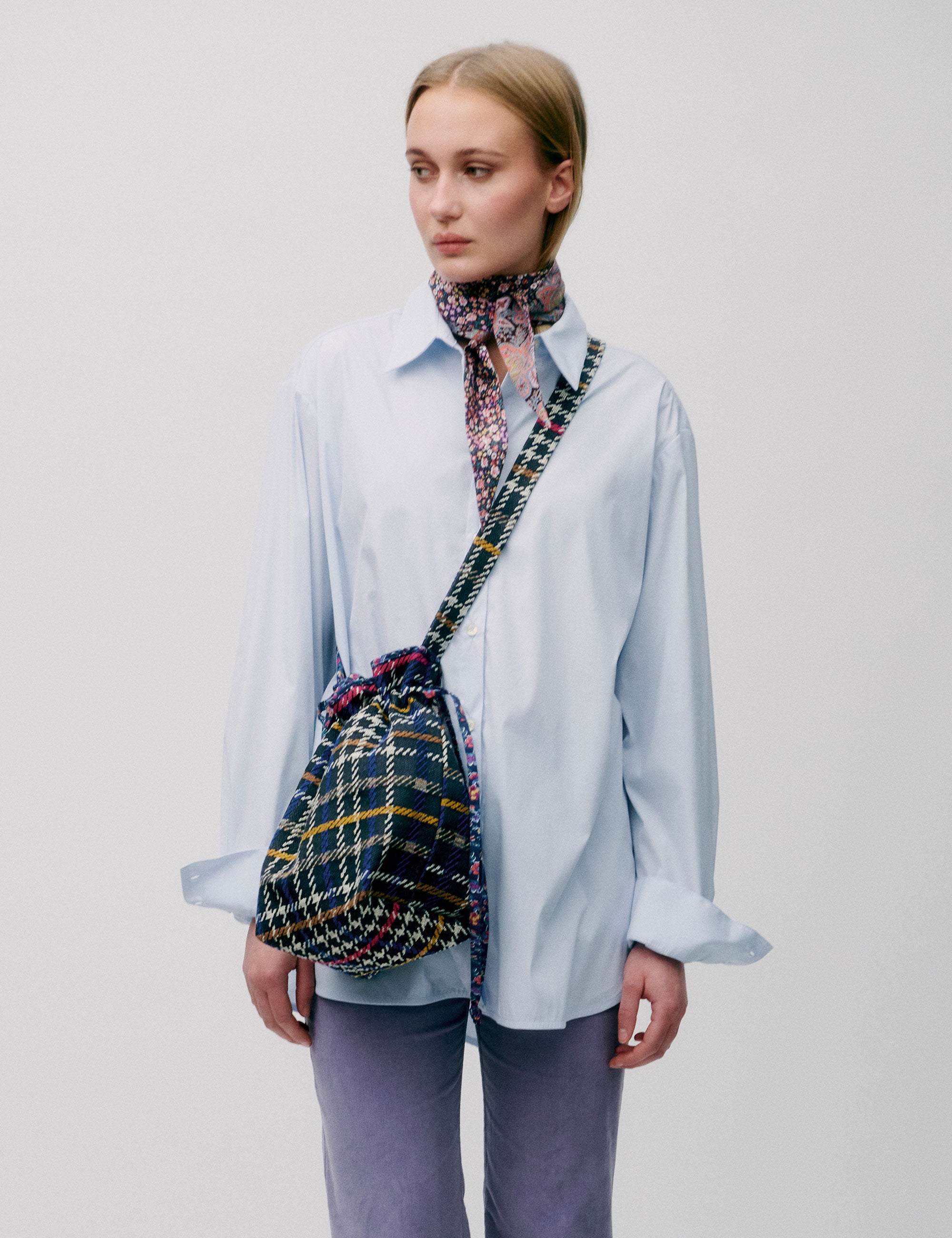 Woman in light blue shirt and lavender colored pants with a check patterned crossbody bag on her shoulder