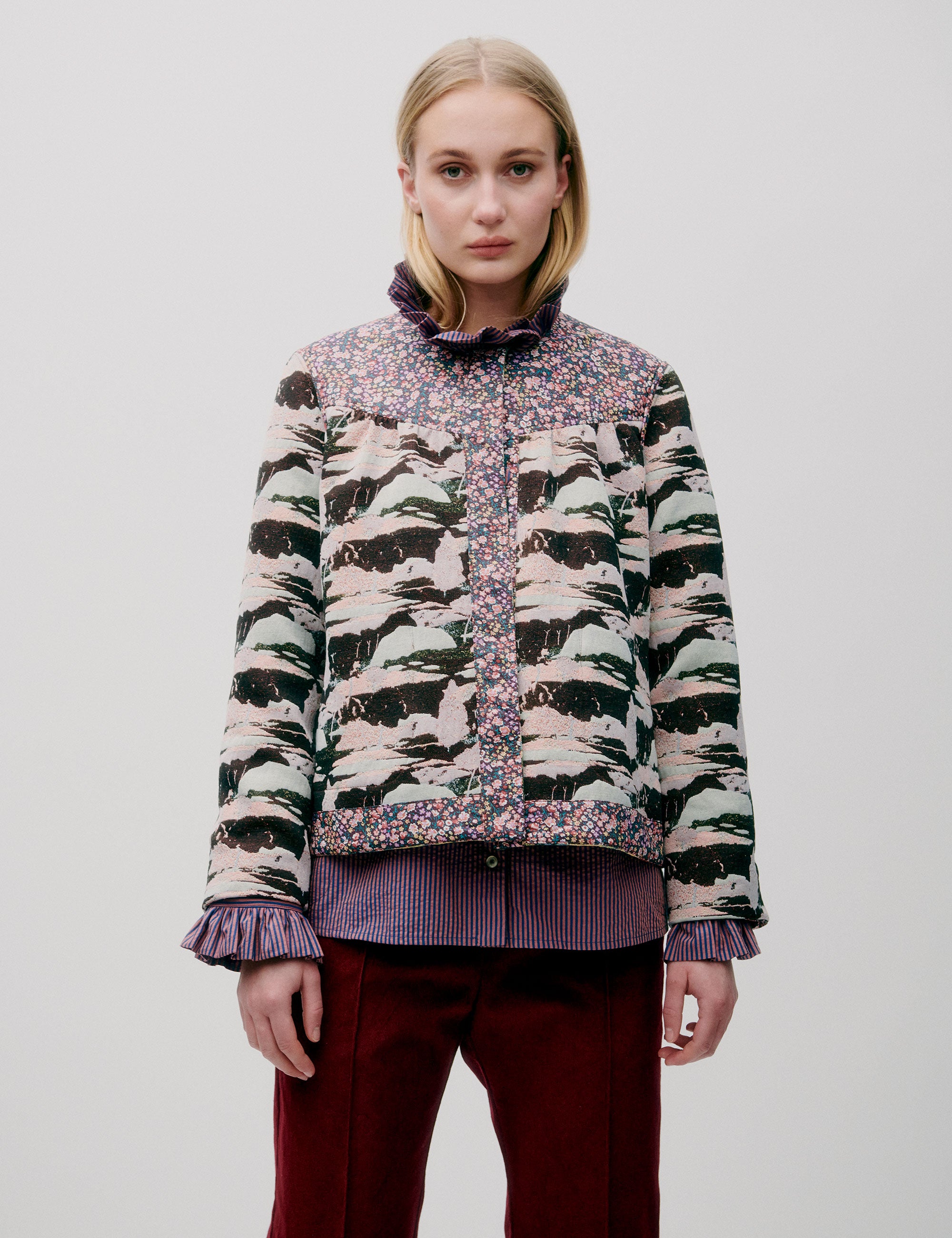 Woman in burgundy colored pants, pink striped shirt with frills and quilted jacket with floral and artistic print