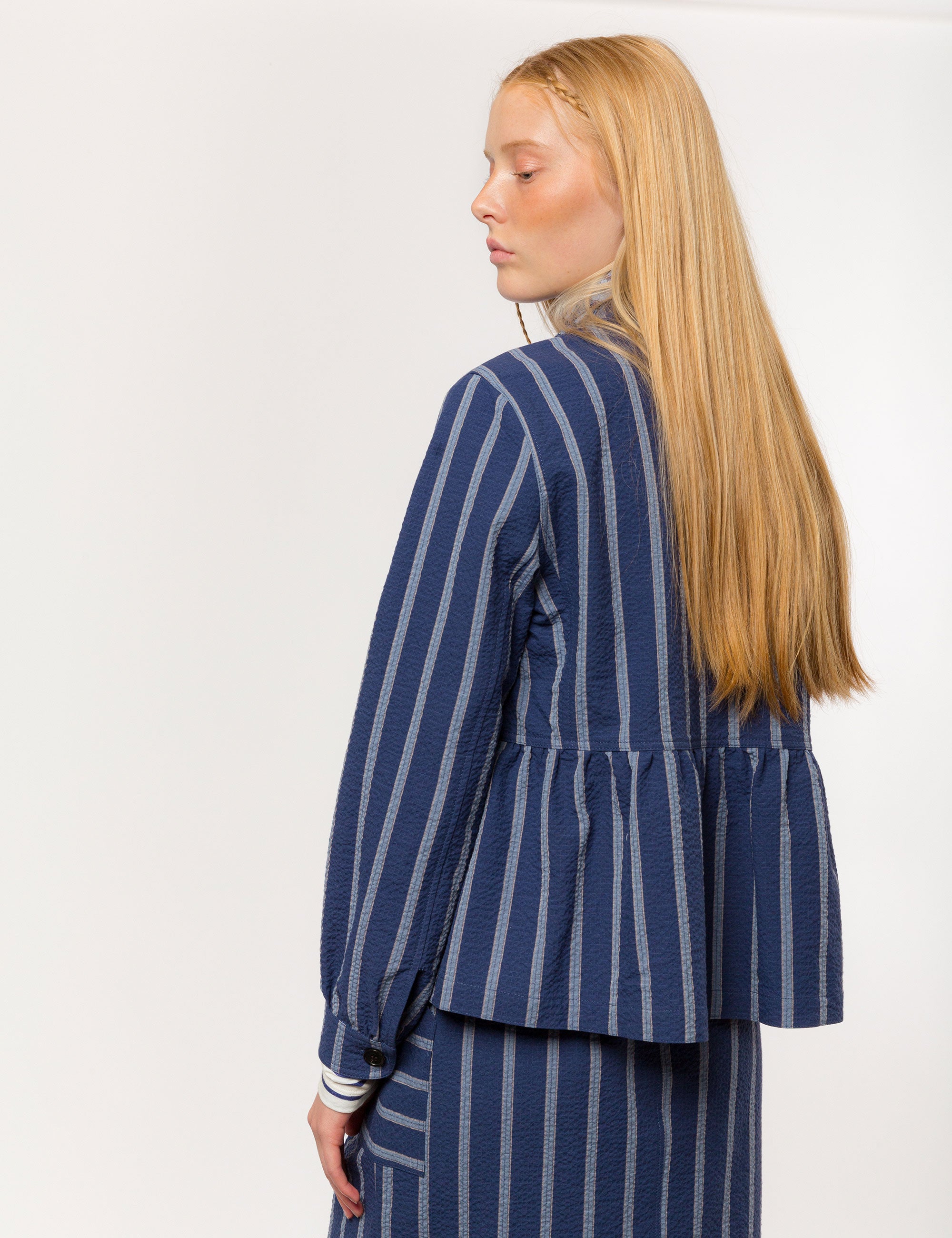 Woman in white and blue striped long sleeved women's jacket with buttons and round neck and matching skirt with pockets