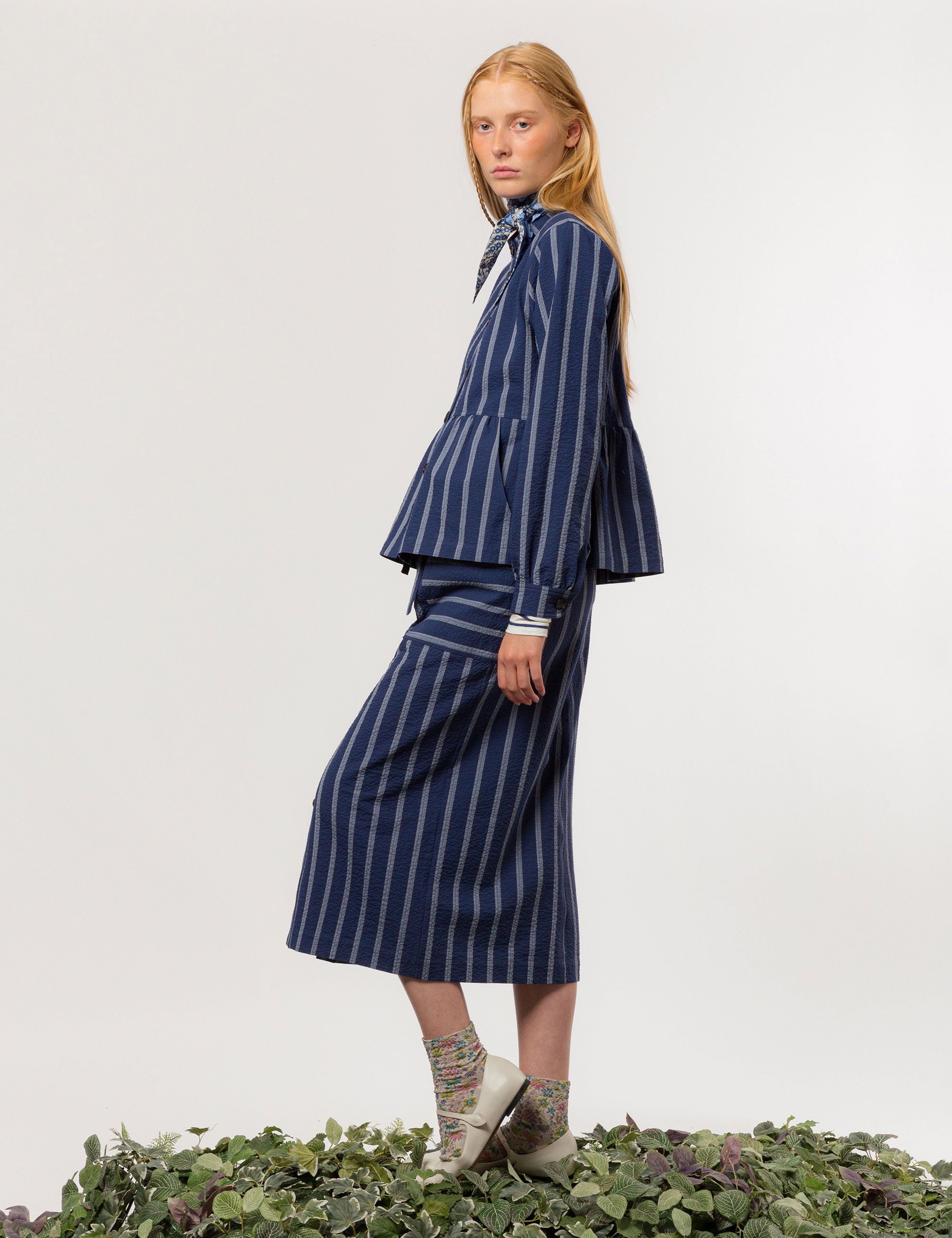 Woman in white and blue striped long sleeved women's jacket with buttons and round neck and matching skirt with pockets