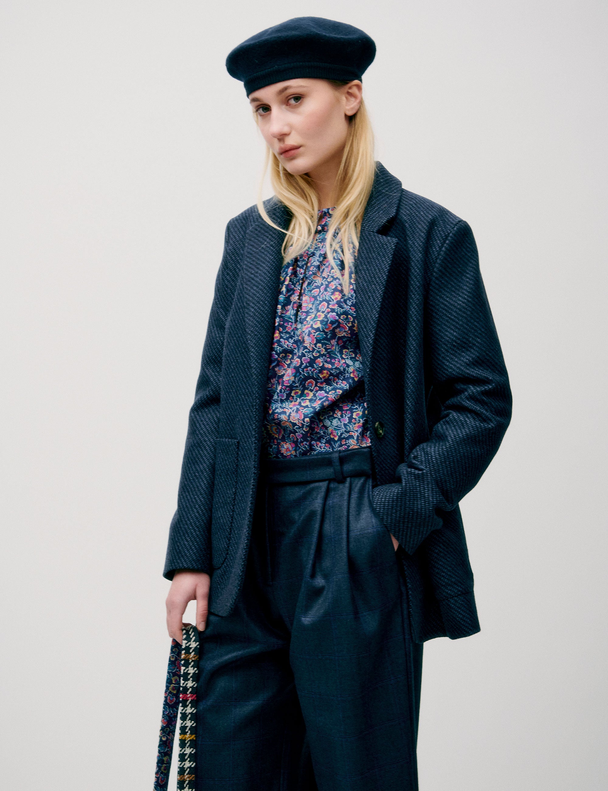 Woman in dark blue wide wool pants, flower patterned blue and pink shirt, dark blue wool jacket with pockets and blue beret