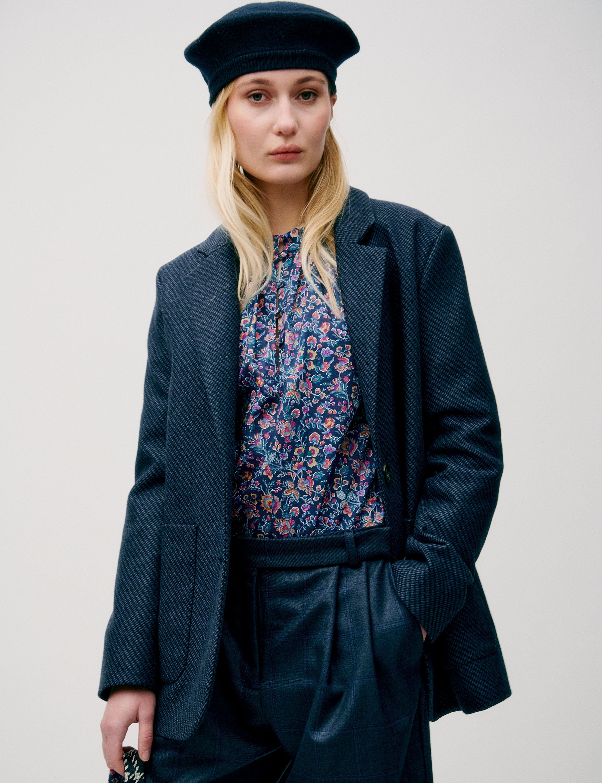 Woman in dark blue wide wool pants, flower patterned blue and pink shirt, dark blue wool jacket with pockets and blue beret